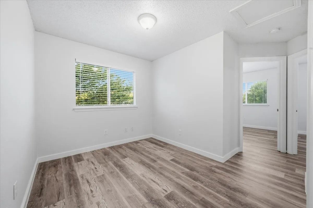 Room featuring wood-finish flooring, a window with blinds, and white walls