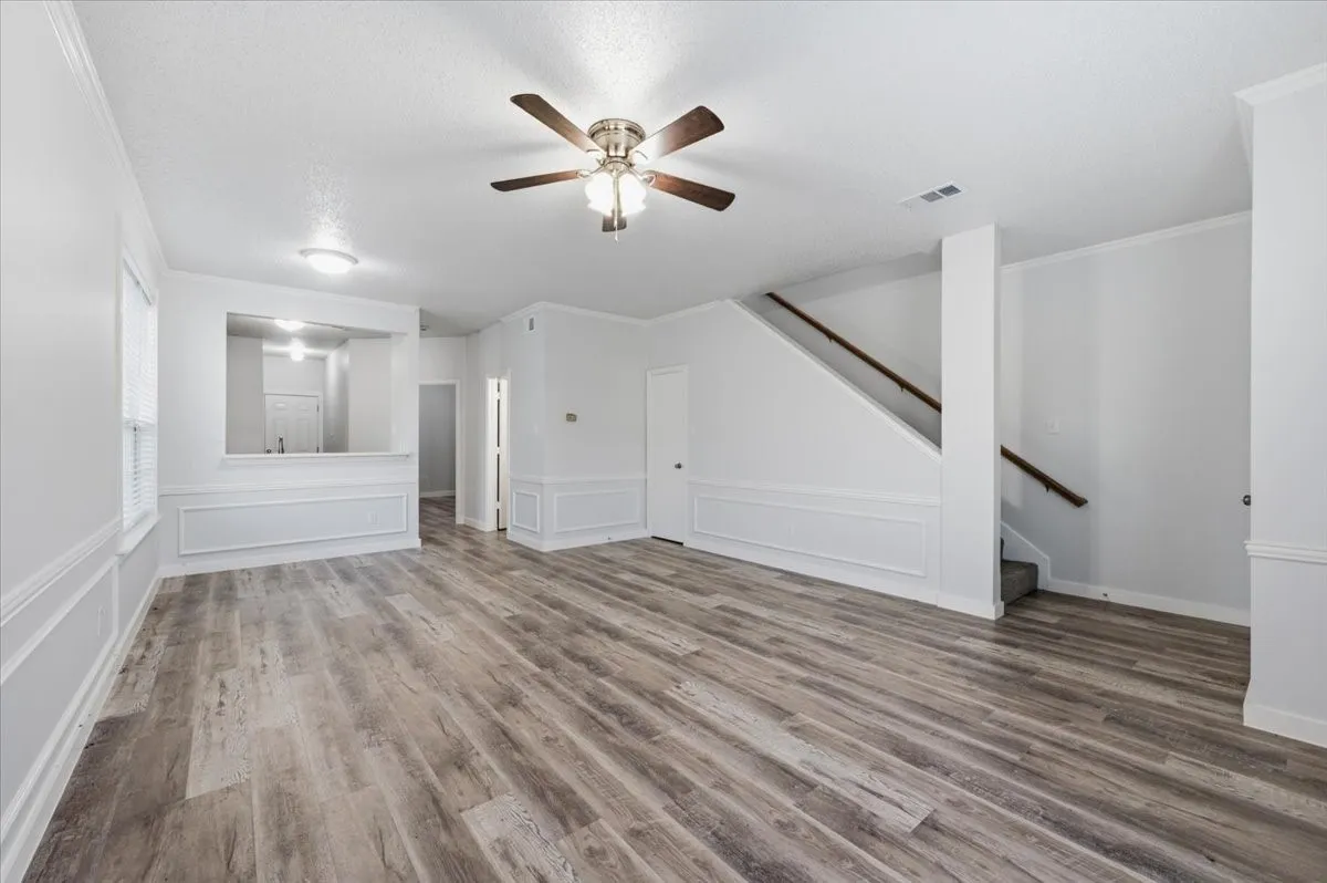 Spacious living area featuring wood-finish flooring, a ceiling fan with integrated lighting, and white wainscoting