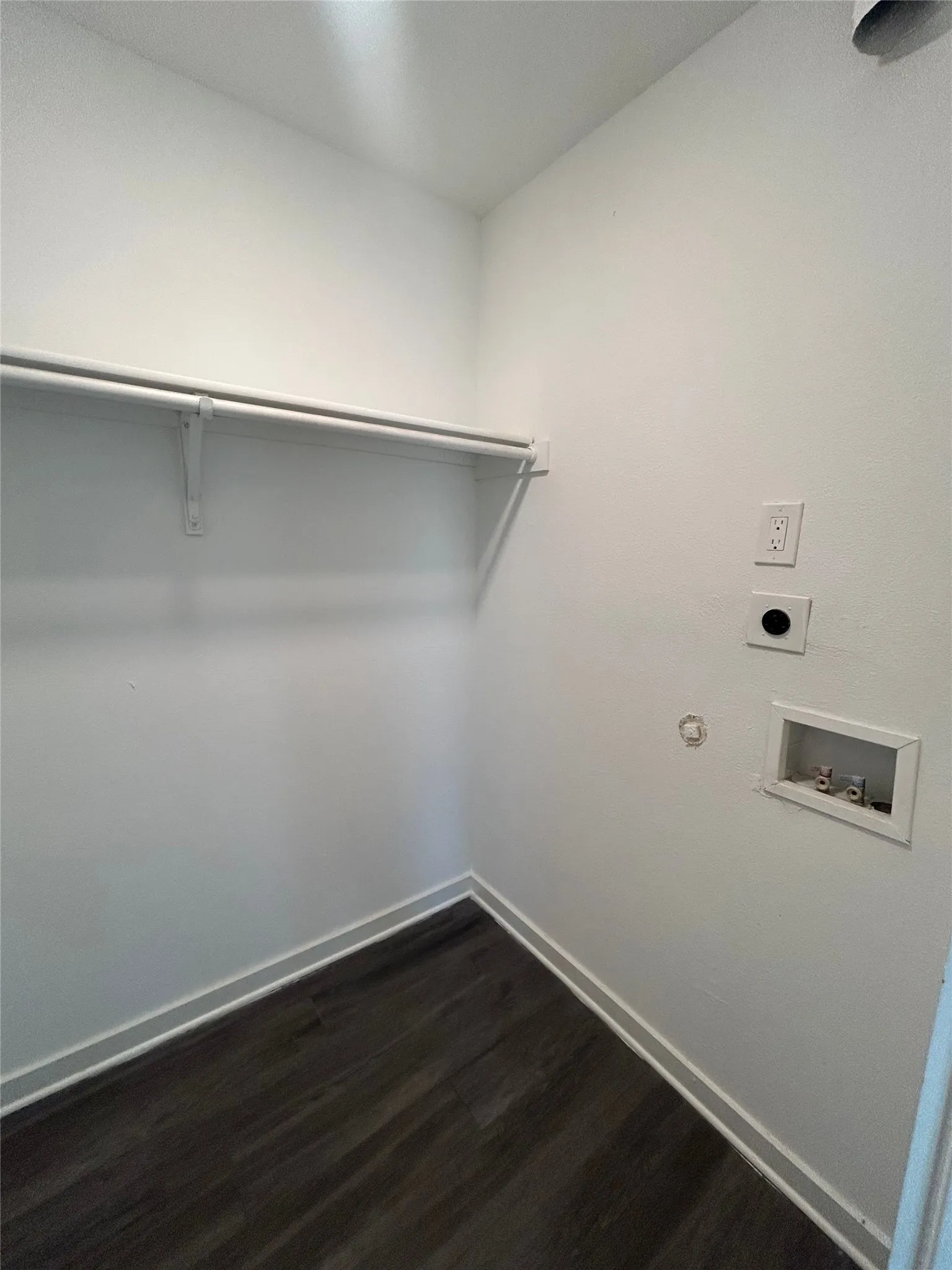 Dedicated laundry area featuring a storage rod, wall-mounted outlets, and wood-finish flooring