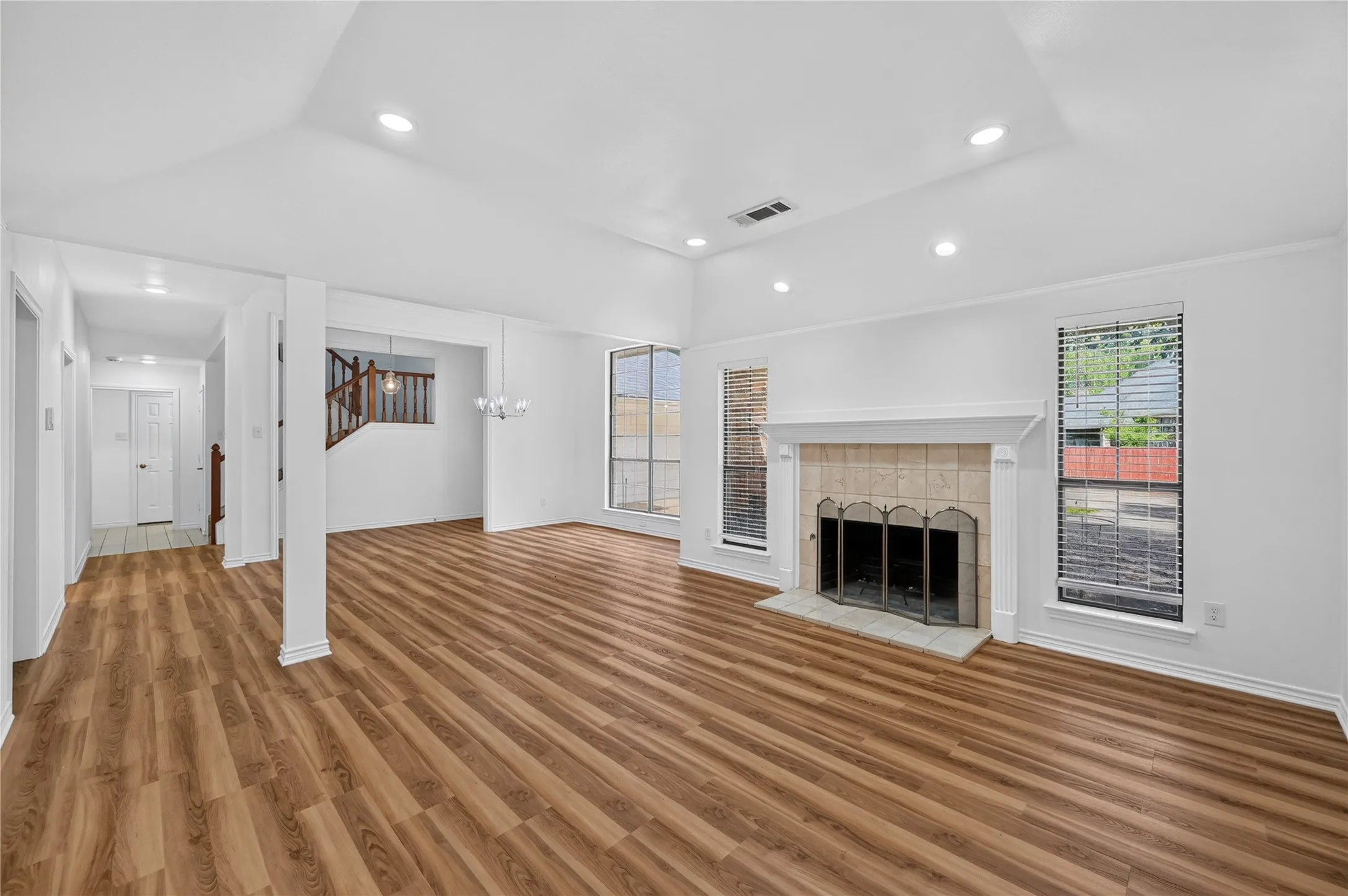 Spacious living area featuring wood-finish flooring, a tiled fireplace with a mantel, recessed lighting, and large windows