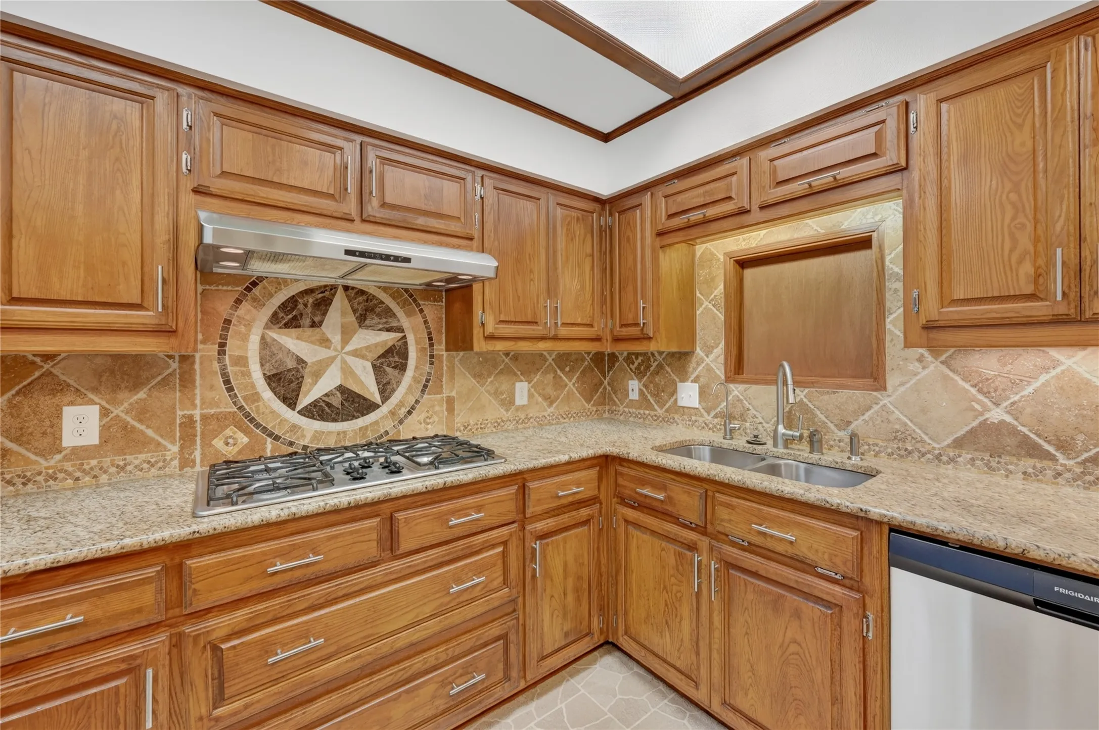 Kitchen featuring wood cabinetry, light-toned countertops, a stainless steel gas cooktop, a stainless steel range hood, and a dual-basin sink