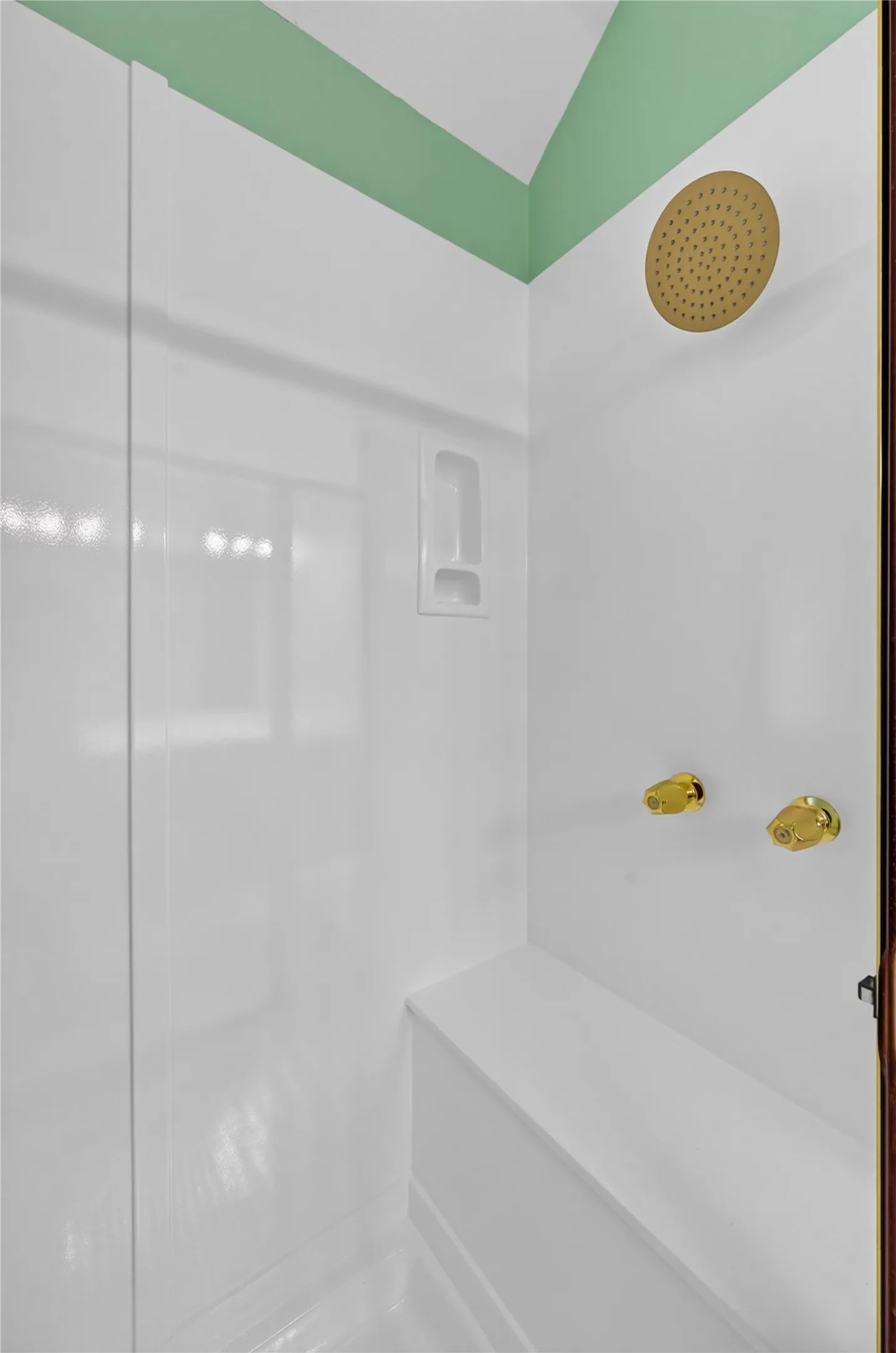 Shower enclosure with an integrated bench, featuring a gold-finish rainfall showerhead and coordinating gold-finish controls