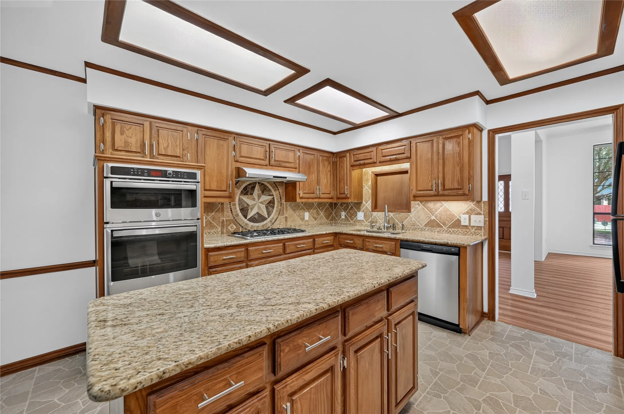 Kitchen featuring a central island with granite countertops, wood cabinetry, built-in stainless steel double ovens, and a decorative tile backsplash