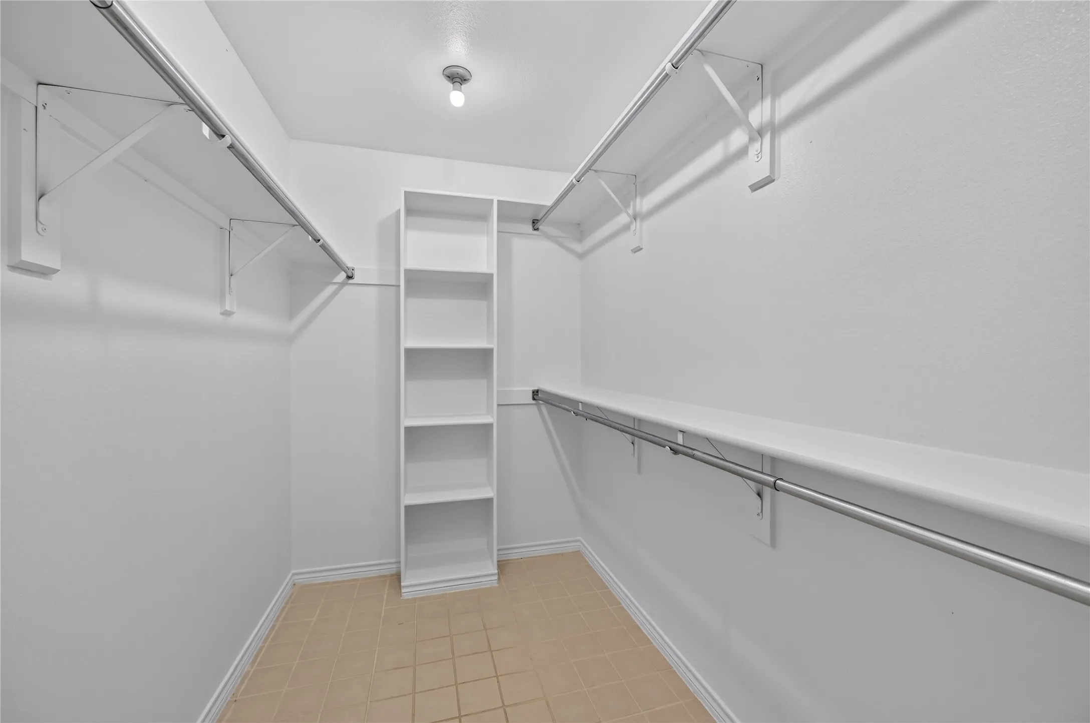 Walk-in closet featuring built-in shelving, multiple hanging rods, and neutral tile flooring