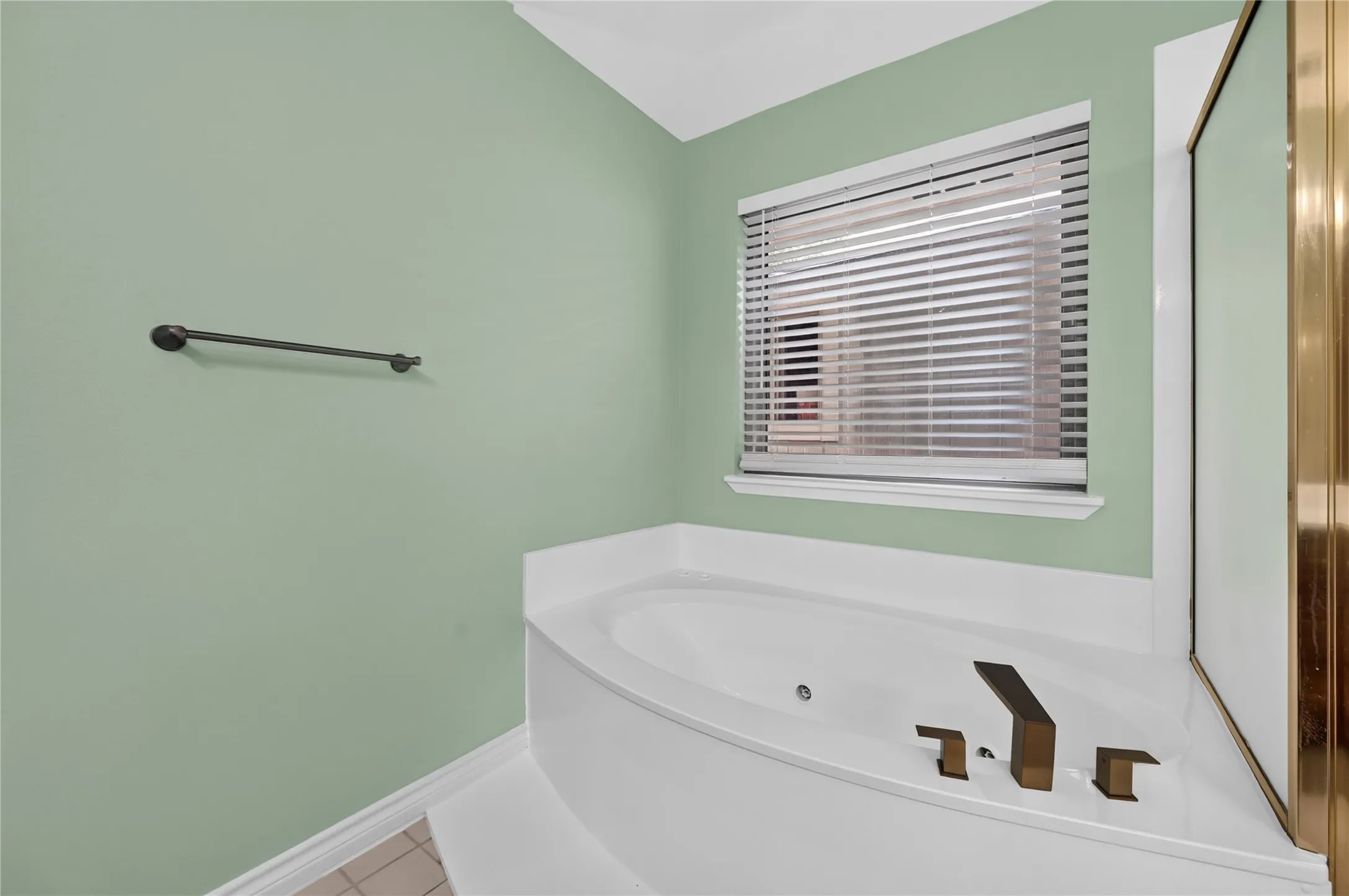White built-in soaking tub with dark bronze fixtures, set against light green walls