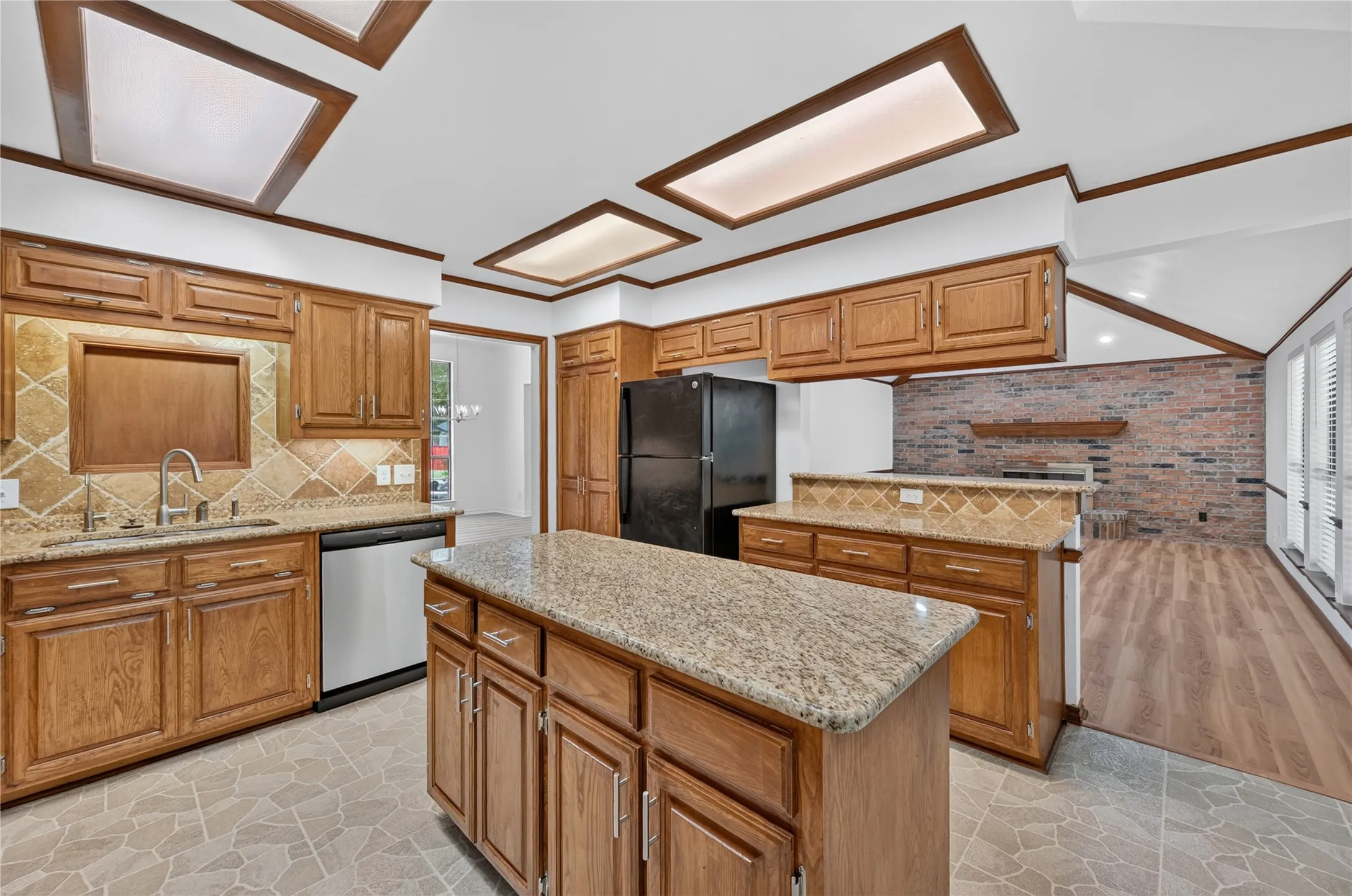 Kitchen featuring wood cabinetry, granite countertops, a center island, stainless steel dishwasher, and a tile backsplash