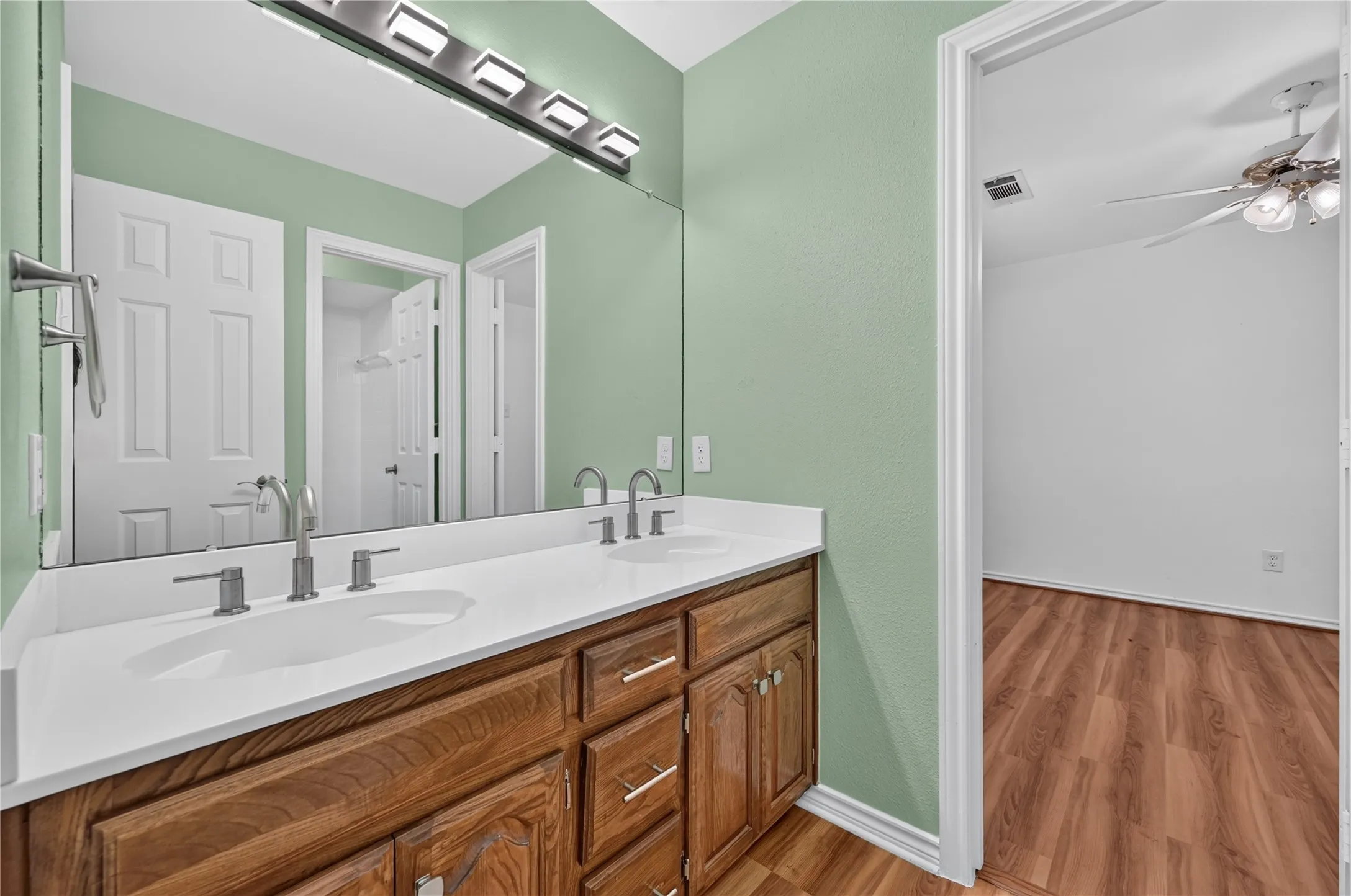 Bathroom featuring a dual-sink vanity with white countertops, wood cabinetry, and brushed nickel fixtures