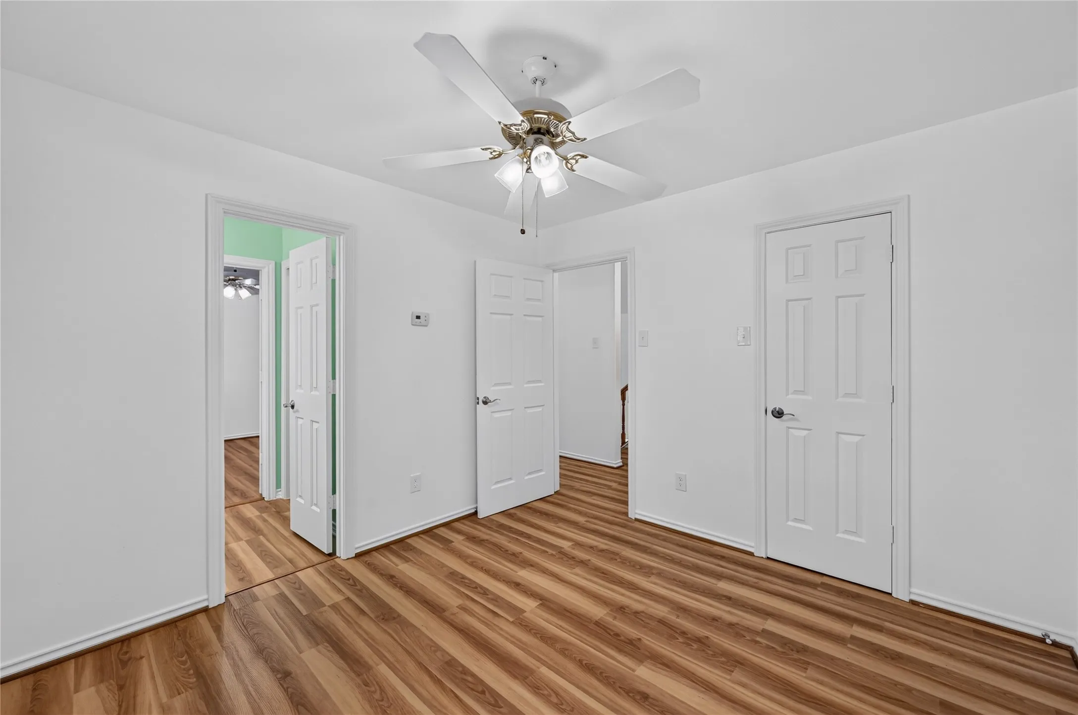Interior space with wood-finish flooring, white walls, and a ceiling fan with integrated lighting