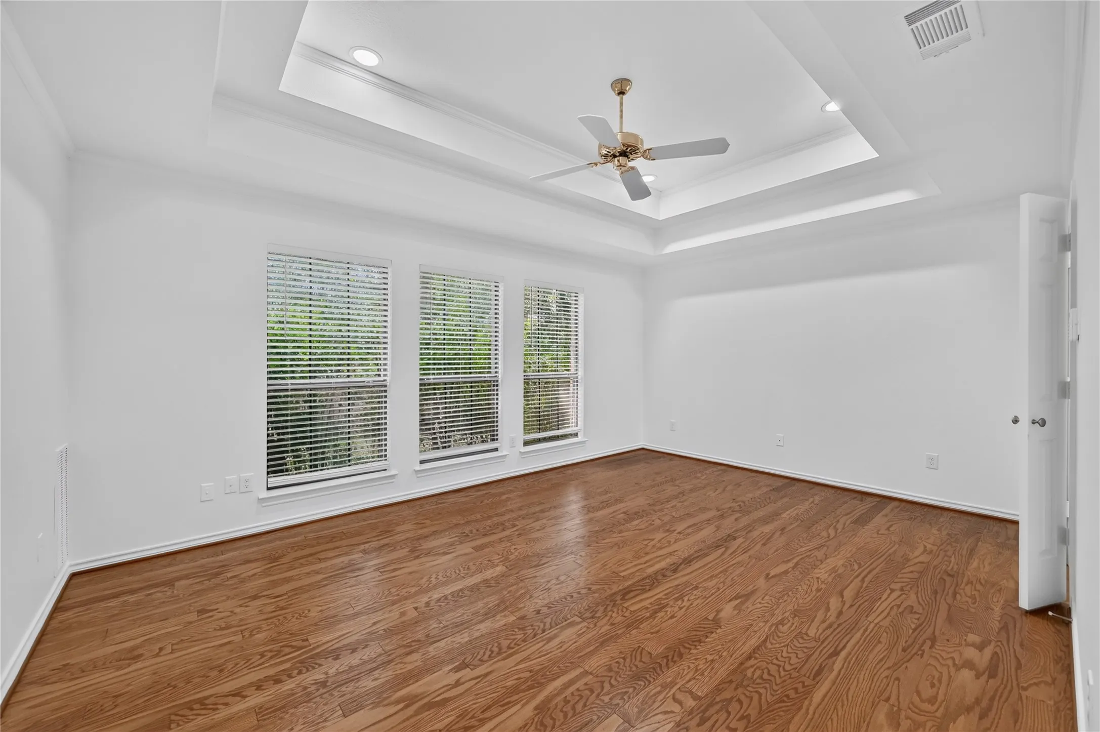 Spacious room featuring wood-finish flooring, a tray ceiling with recessed lighting, and a ceiling fan