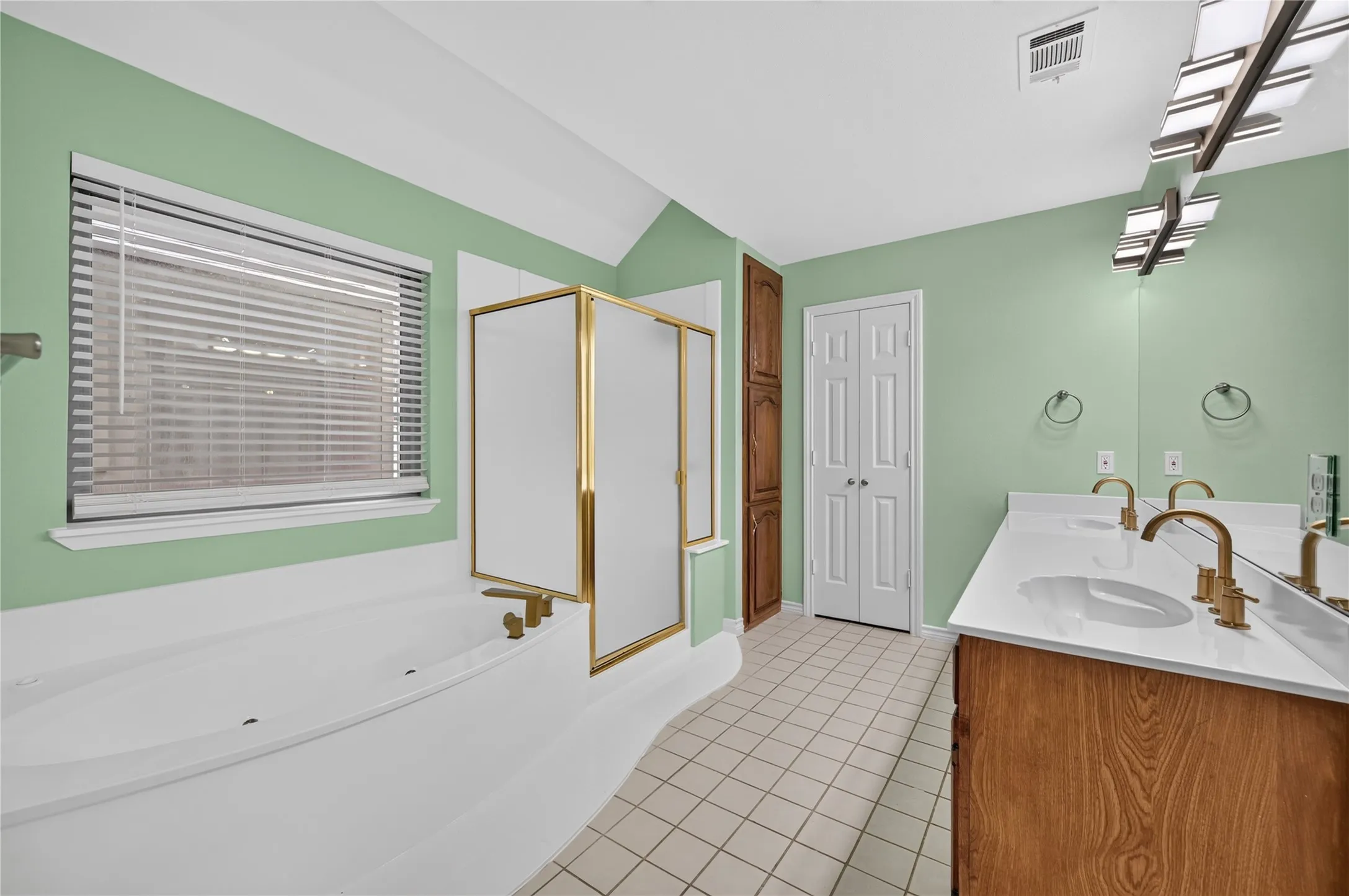 Bathroom featuring a built-in tub, separate shower with brass-finish framing, dual vanity with white countertops, and wood-finish cabinetry