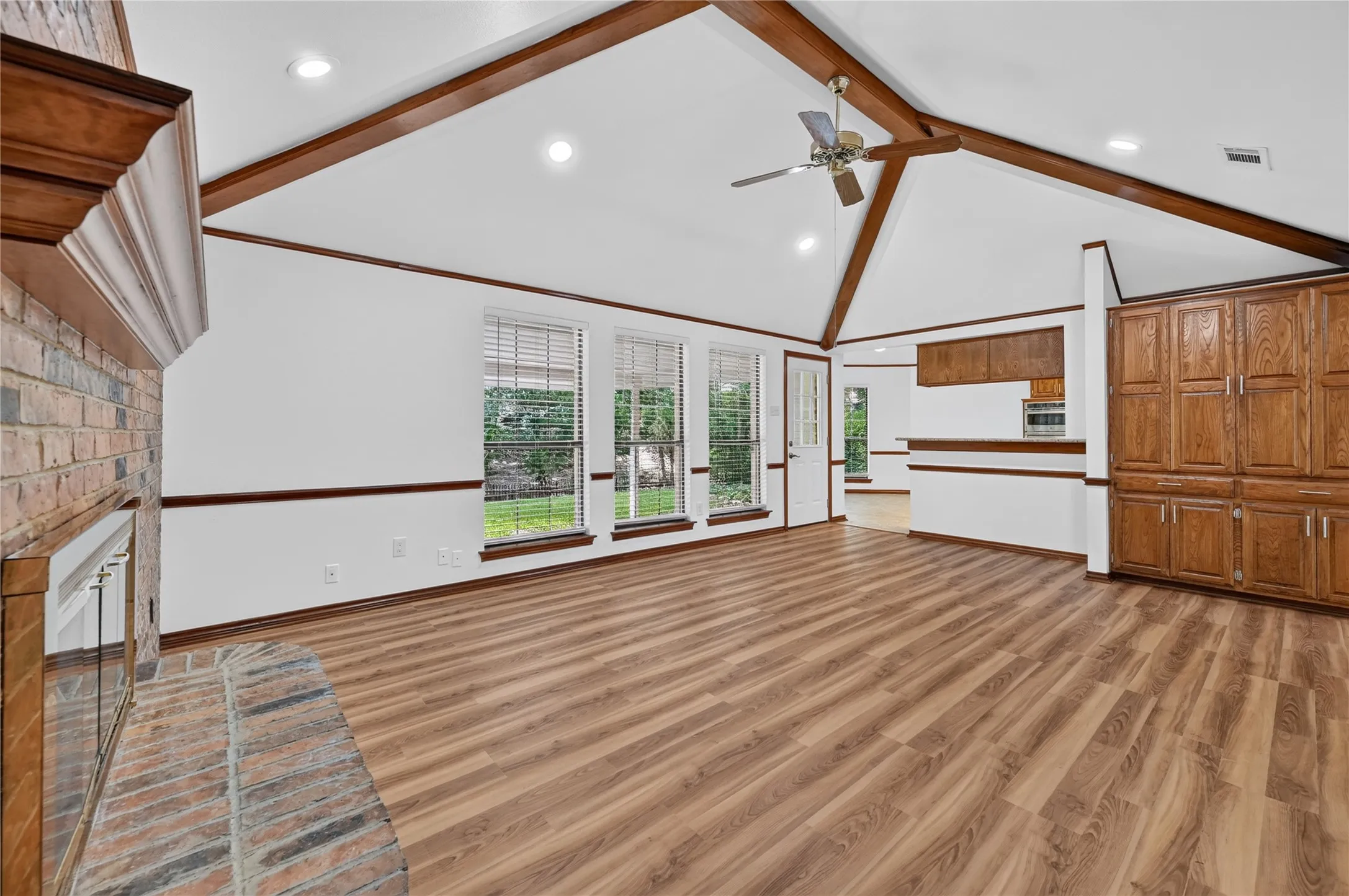 Spacious living area featuring a vaulted ceiling with exposed wood beams, wood-finish flooring, and a brick fireplace with a wood mantel