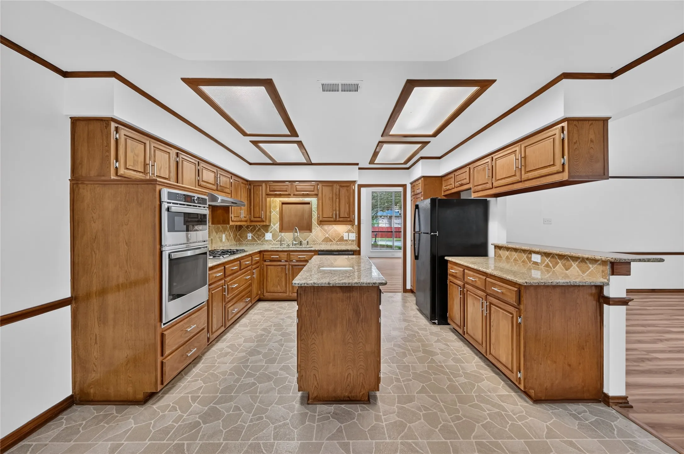 Kitchen featuring wood cabinetry, stainless steel double wall ovens, a central island with a granite-style countertop, and patterned tile flooring