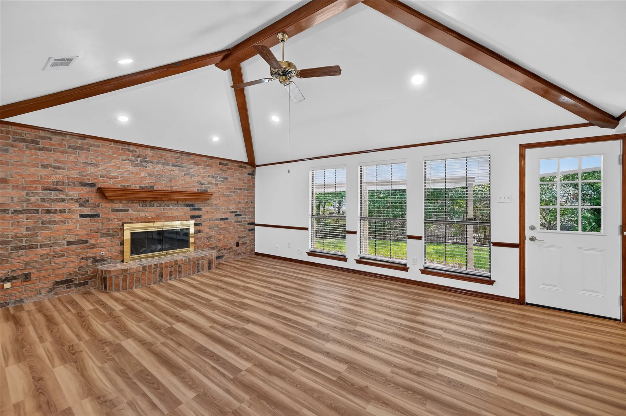 Spacious living area featuring a vaulted ceiling with exposed wood beams, a brick fireplace with a wood mantle, and wood-finish flooring