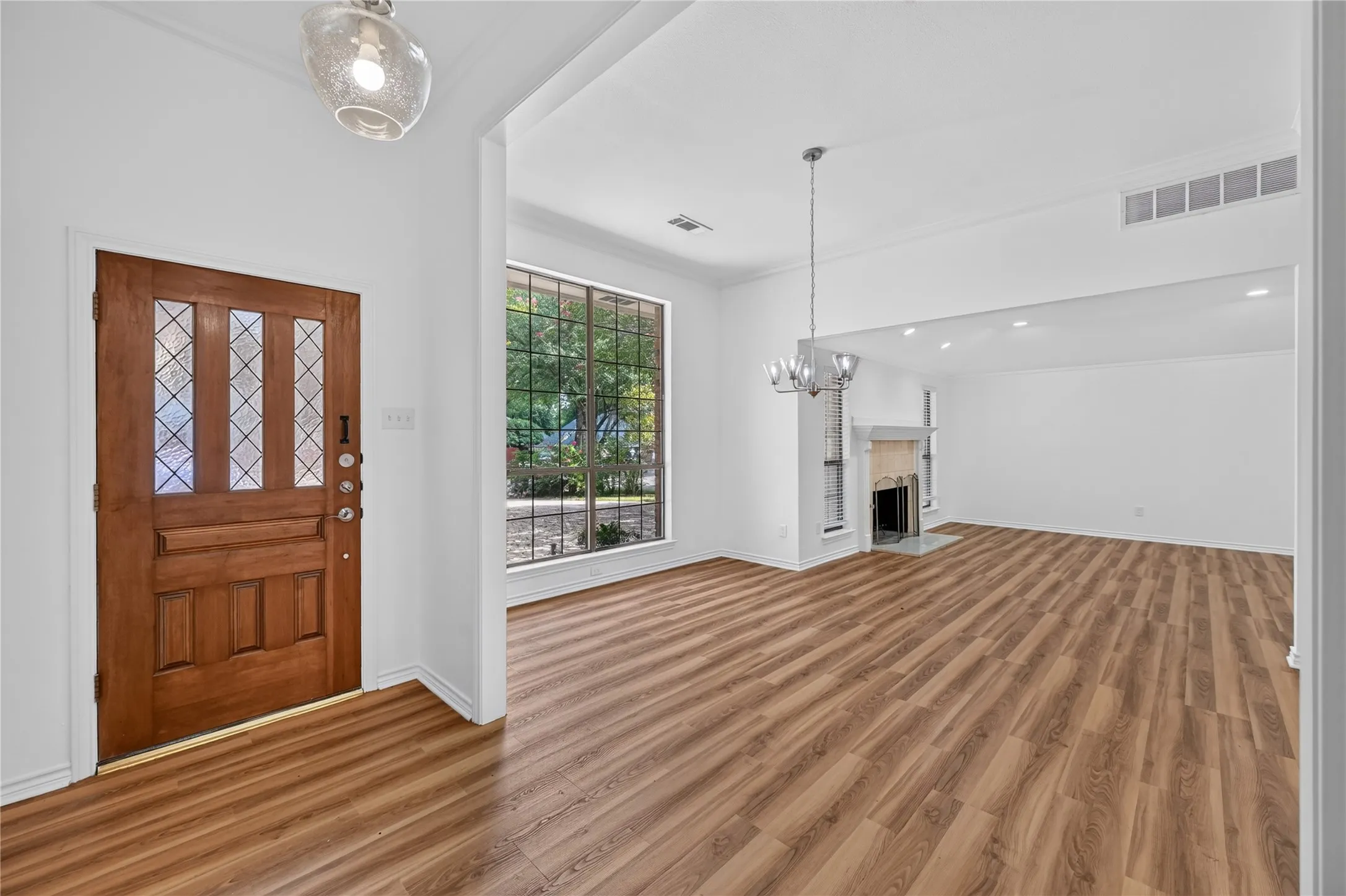 Entryway with wood-finish flooring, a decorative wood door with glass inserts, and an open concept leading to a living area with a fireplace and large picture window