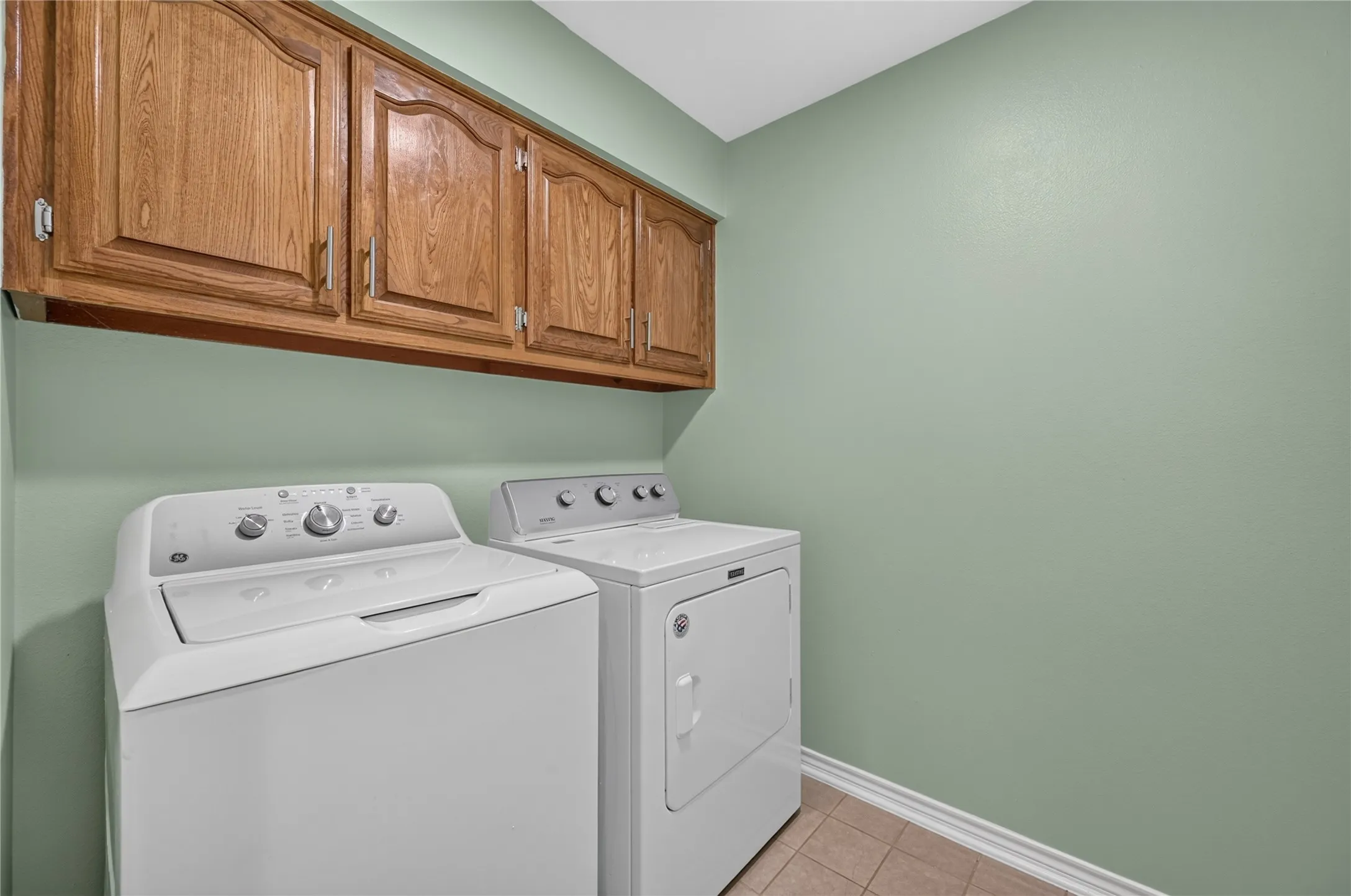 Utility area featuring wood cabinetry, light green walls, and tiled flooring