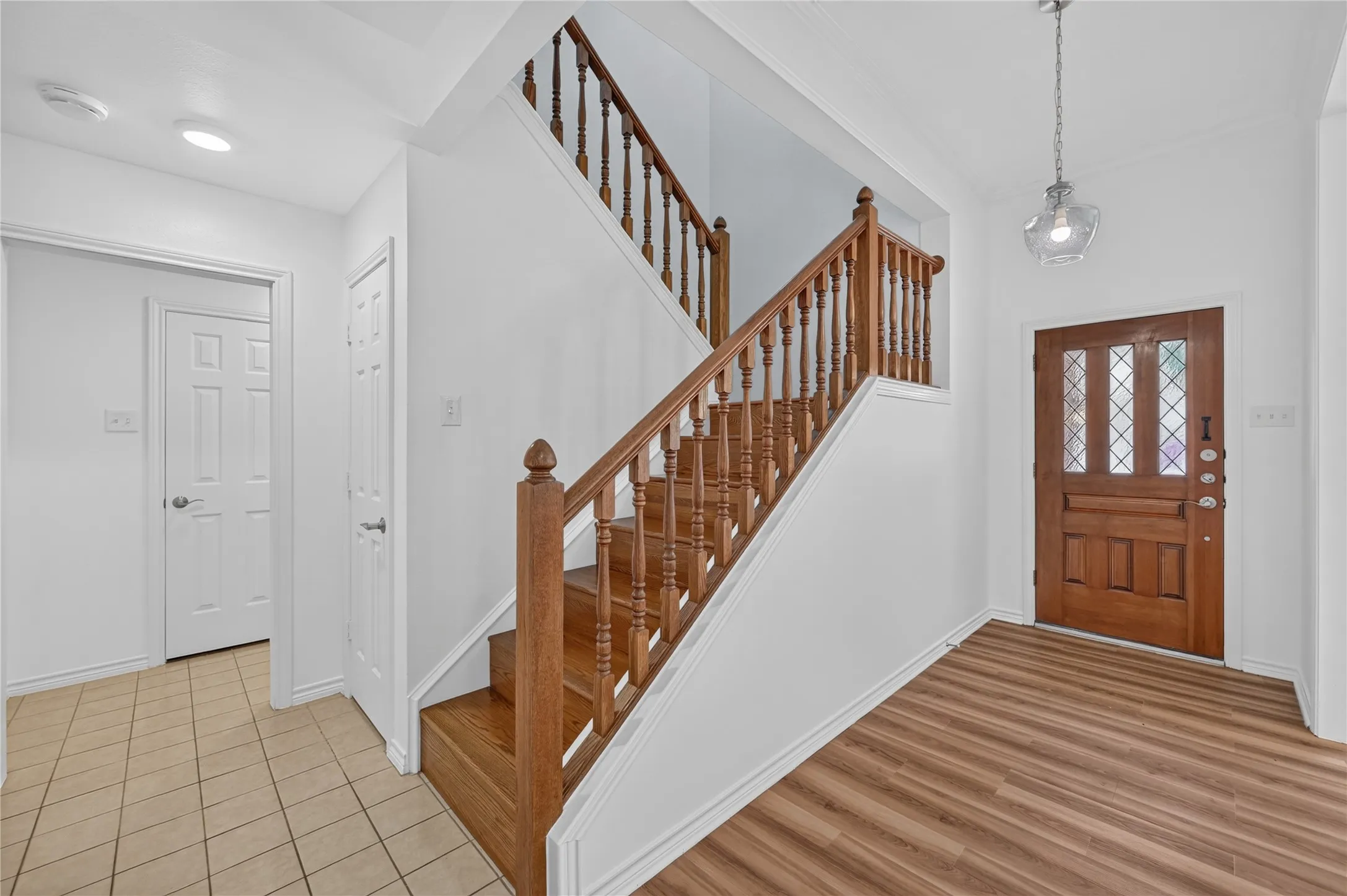 Entry foyer featuring a wood-finish flooring, a classic wooden staircase with balusters, and a solid wood entry door with decorative glass inserts