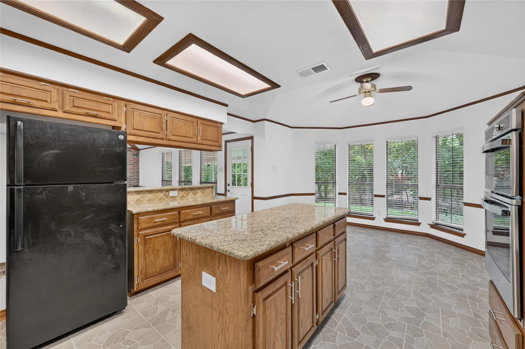 Kitchen featuring a central island with granite countertop, wood cabinetry, tile flooring, and a bay window