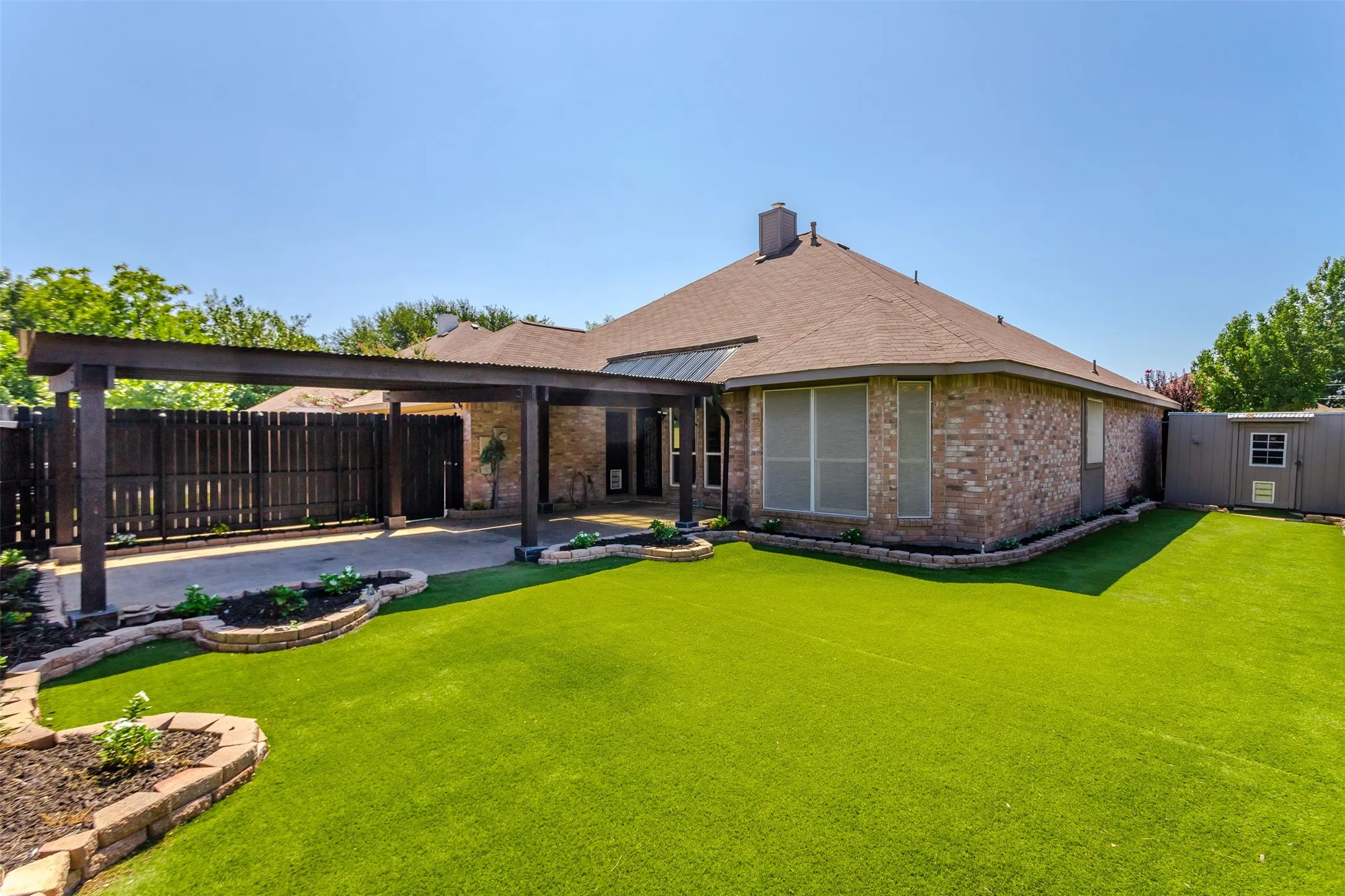 Brick exterior with a covered patio, extensive artificial turf, and a storage shed