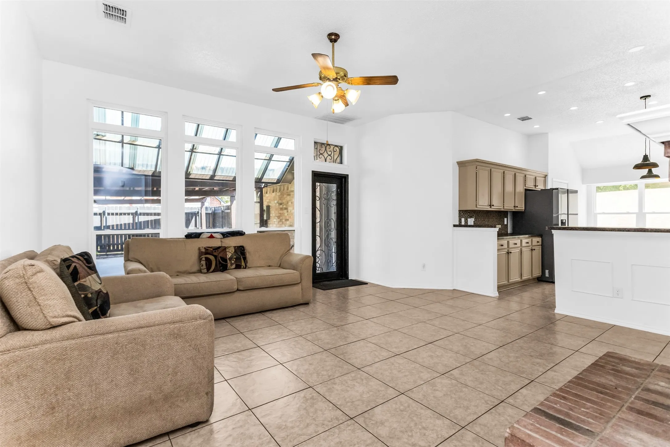 Open-concept living area featuring tile flooring, a ceiling fan with integrated lighting, and abundant natural light from multi-pane windows
