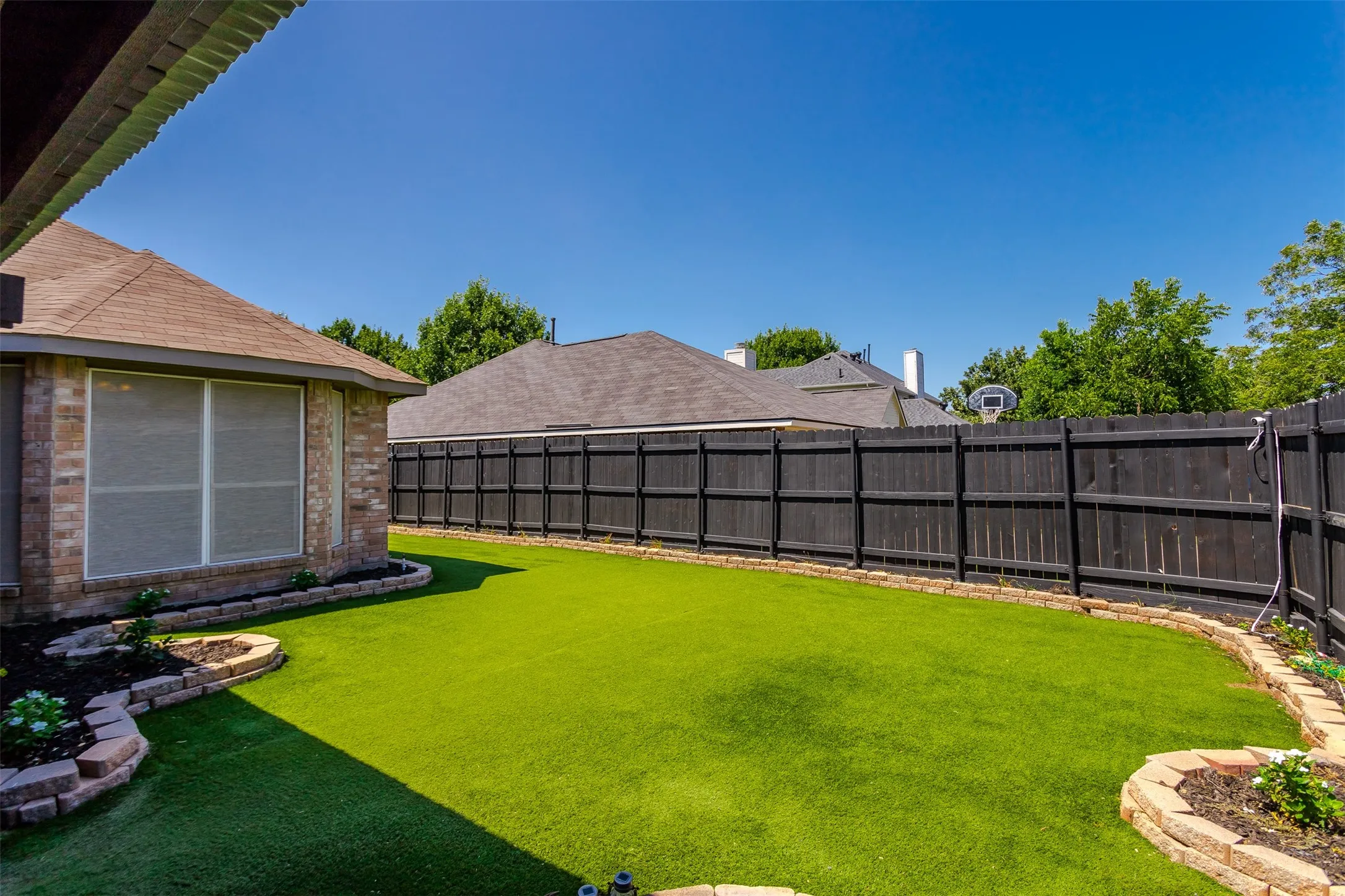 Expansive backyard featuring a lush, manicured lawn bordered by mature landscaping and flowering beds