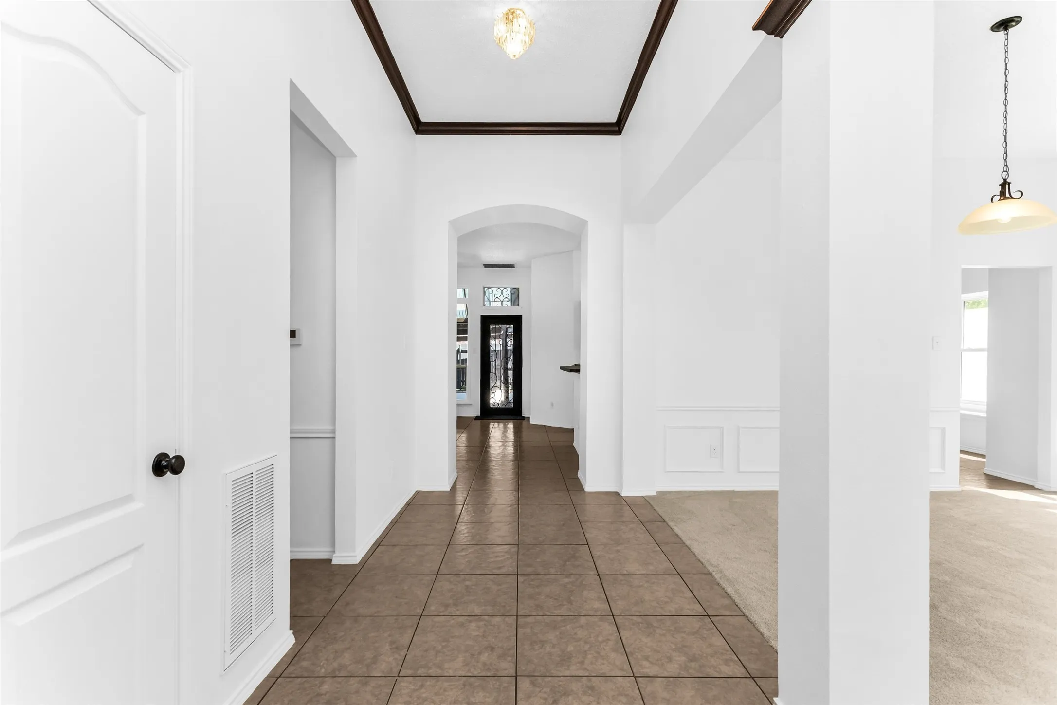 Foyer featuring tile flooring, archways, crown molding, and wainscoting