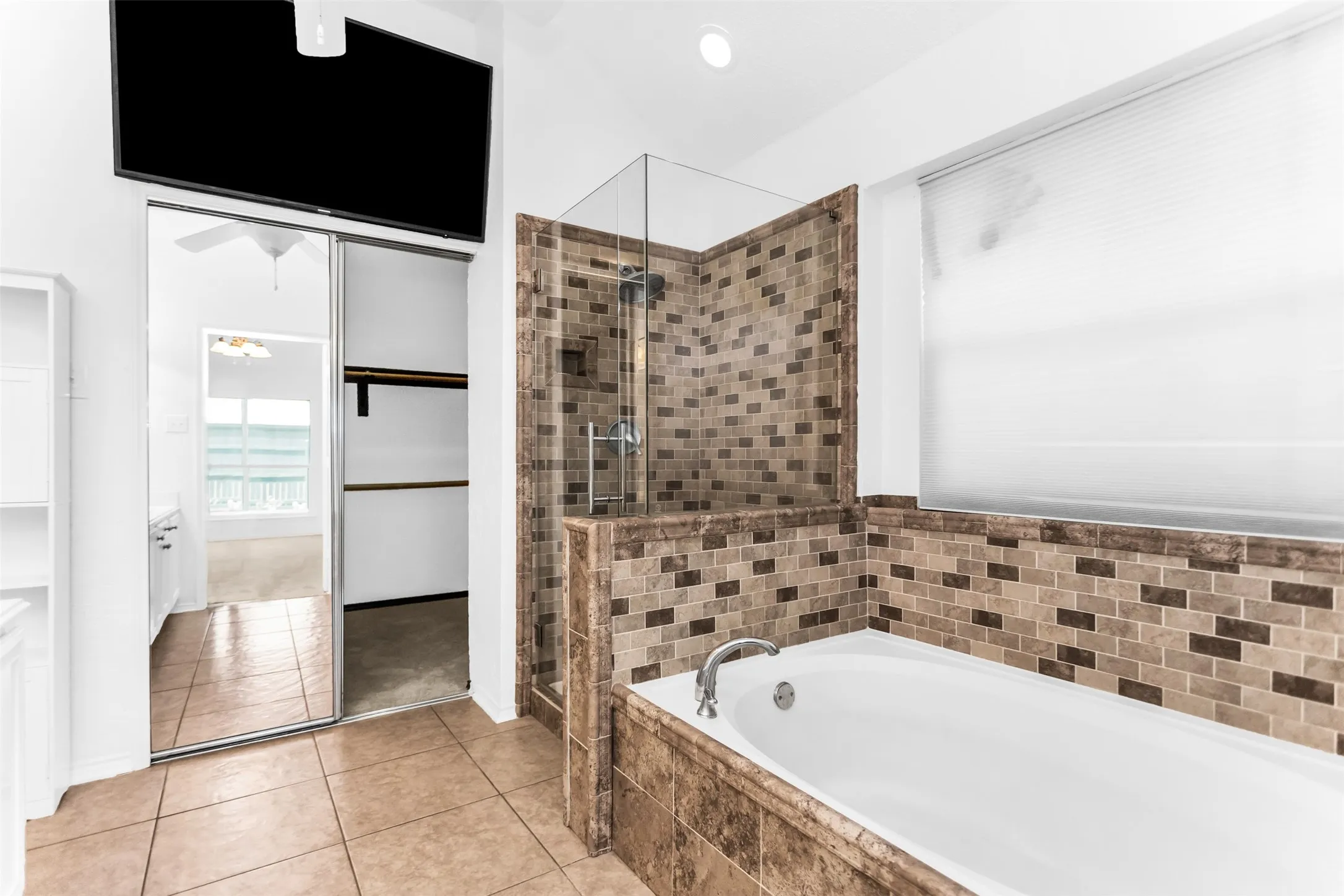Spa-inspired primary bathroom featuring a soaking tub with tile surround, walk-in shower with glass enclosure and mosaic tile walls in warm earth tones, tile flooring, and dual vanity with ample storage