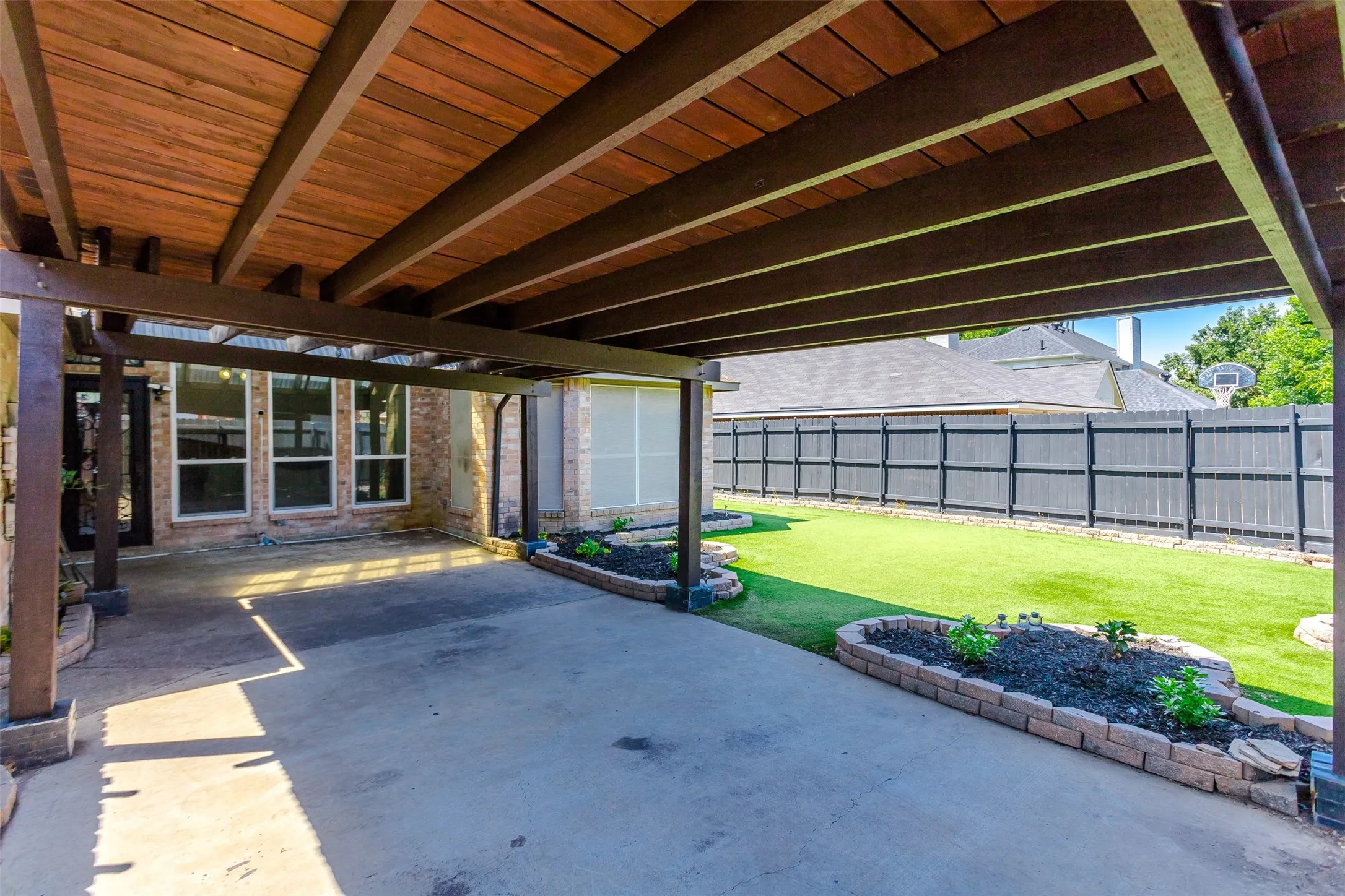 Covered patio featuring a wood-finish ceiling, concrete flooring, and brick-edged planter beds