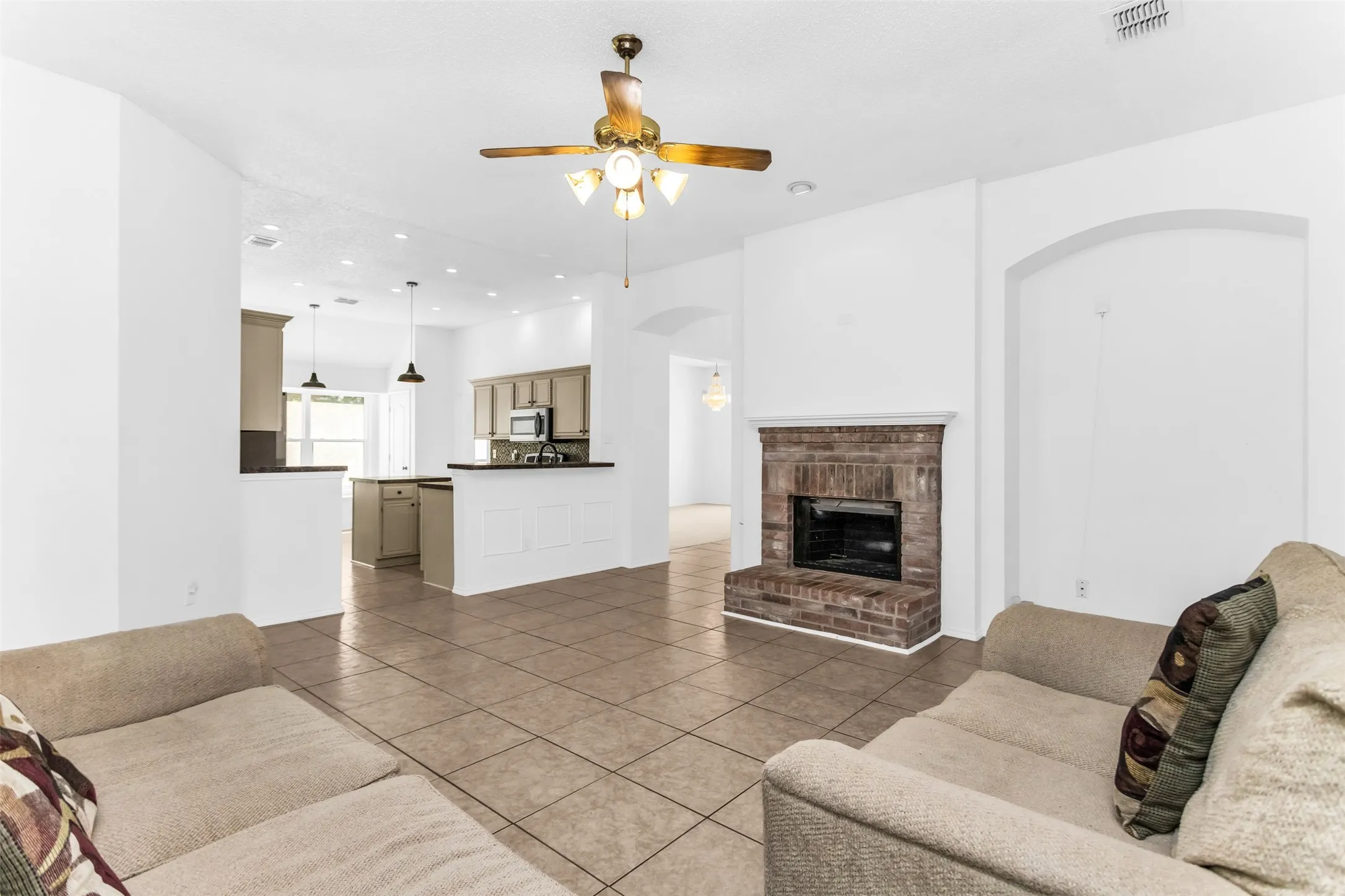 Open-concept living space featuring a brick-surround fireplace, tile flooring, and a ceiling fan with integrated lighting