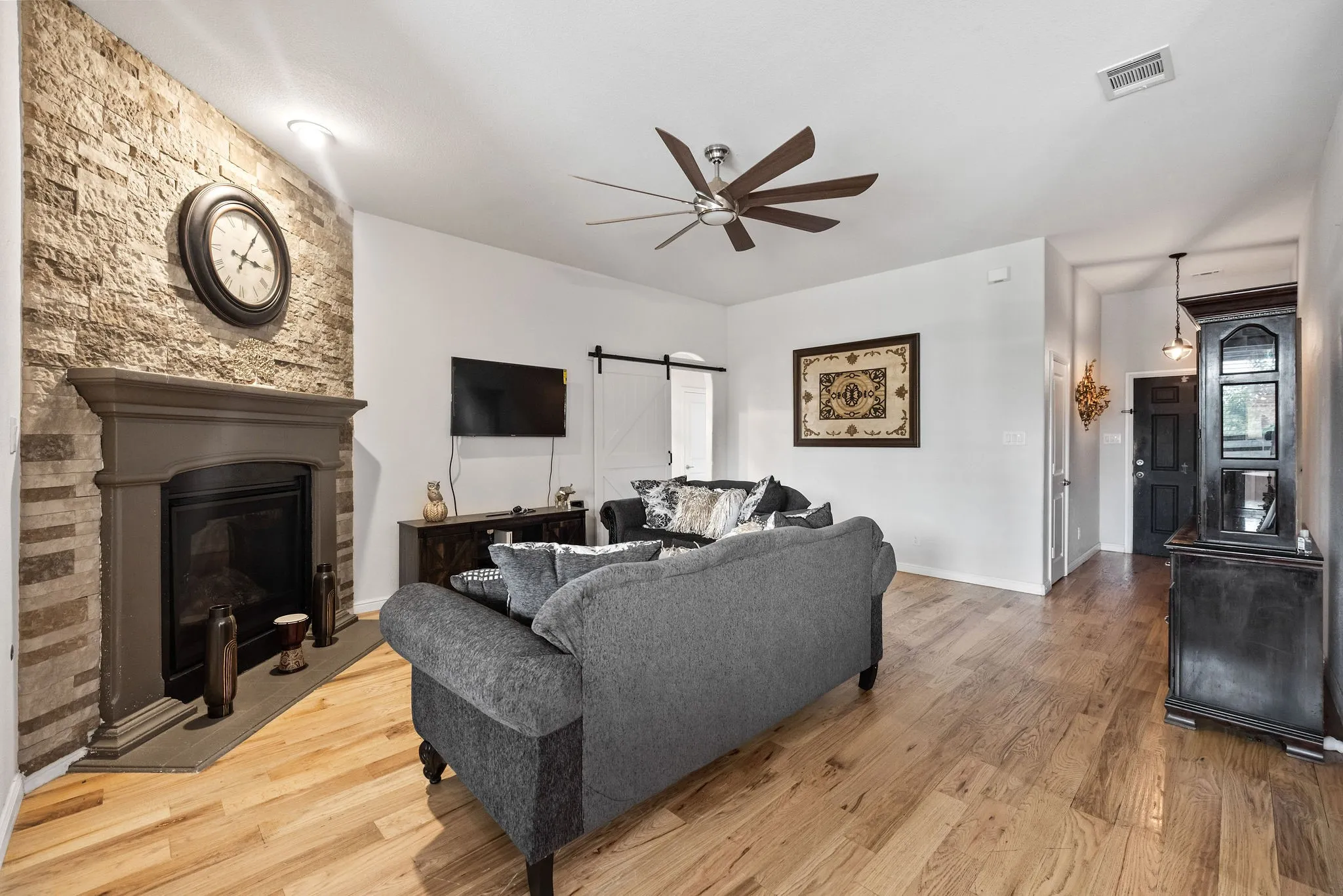 Living area featuring a stone accent wall, fireplace with mantel, hardwood flooring, and a ceiling fan