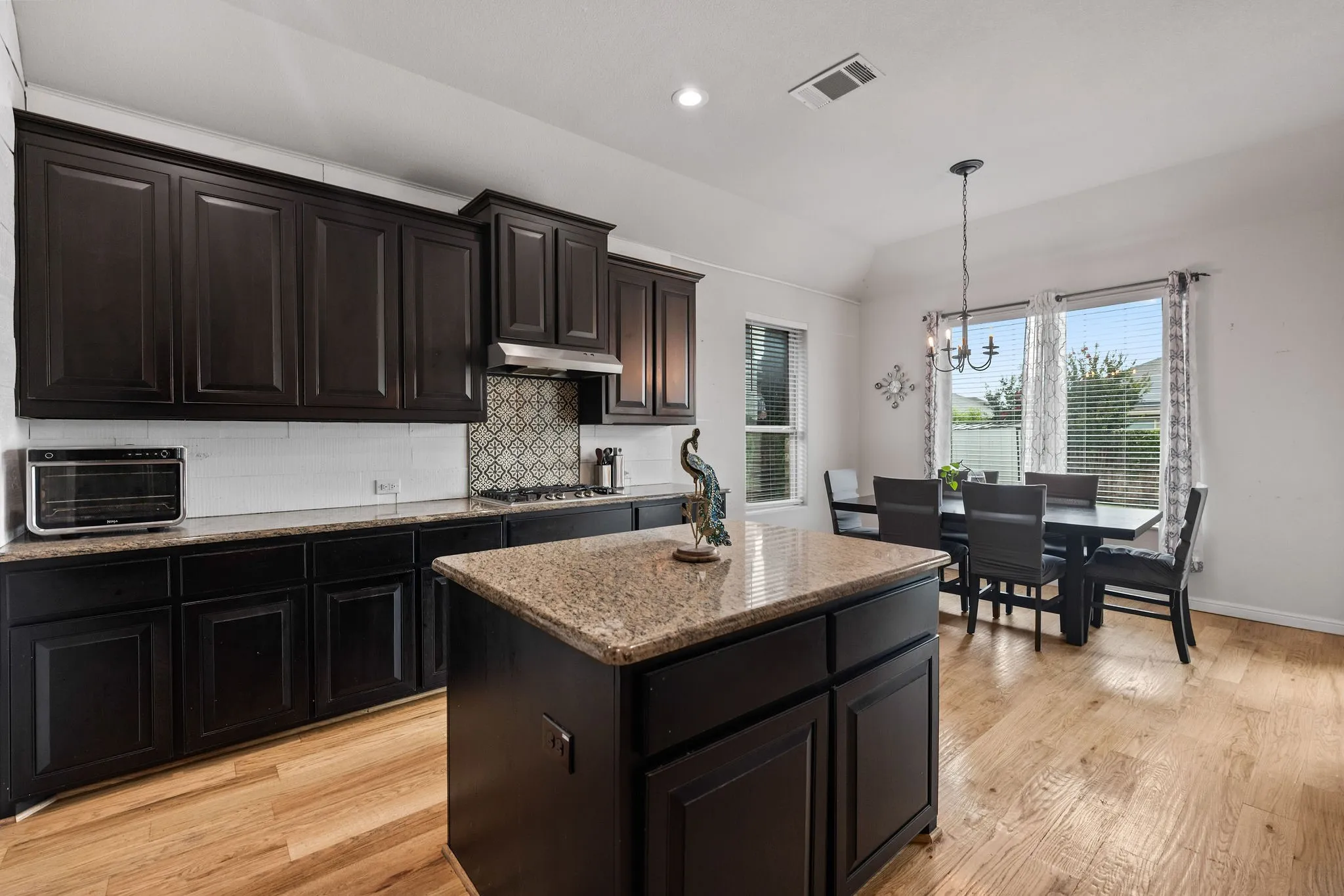 Kitchen and dining area featuring dark wood cabinetry, granite countertops, and wood-finish flooring