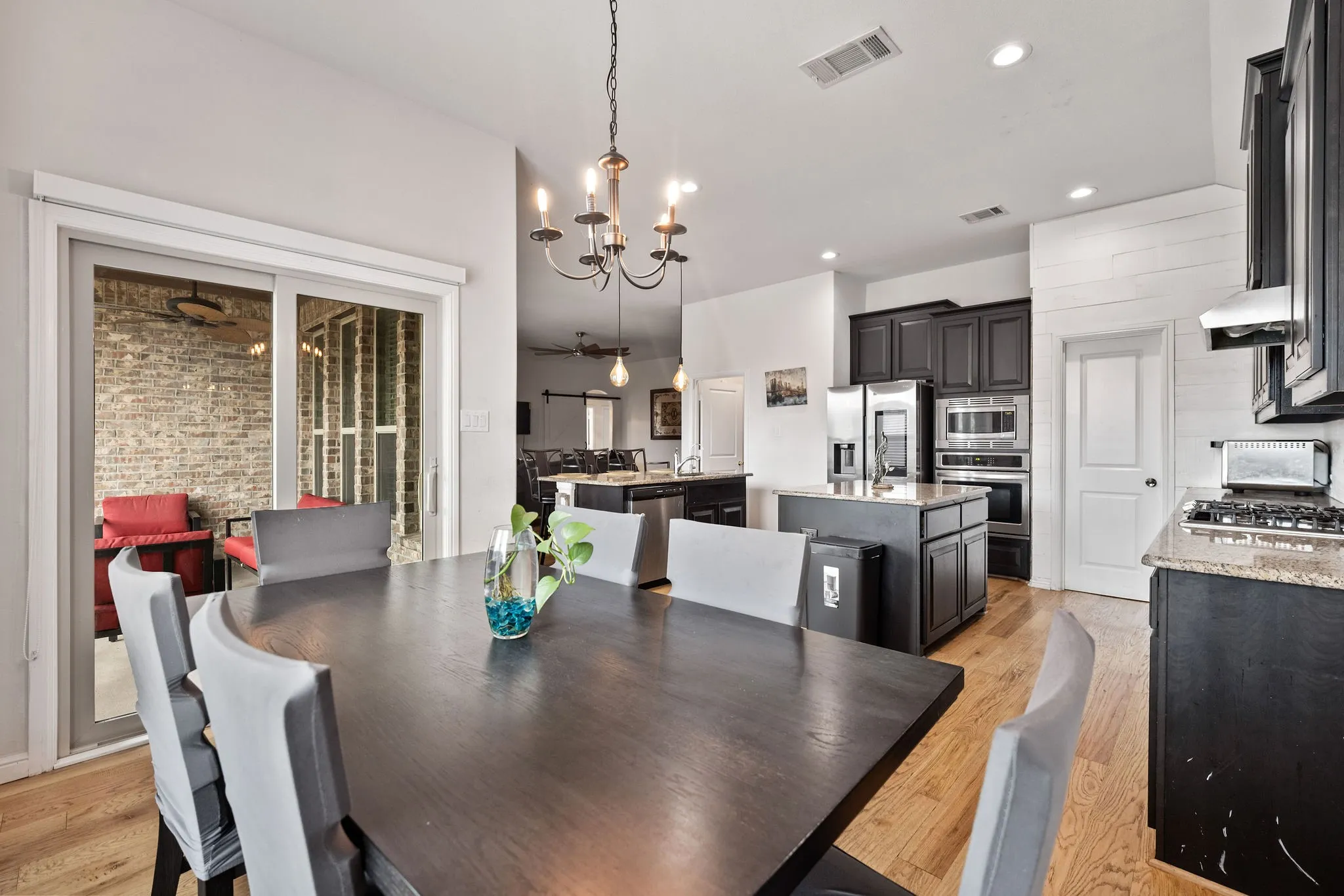 Open-concept living space featuring wood-finish flooring, a contemporary chandelier, and a kitchen with dark cabinetry, stainless steel appliances, and granite countertops
