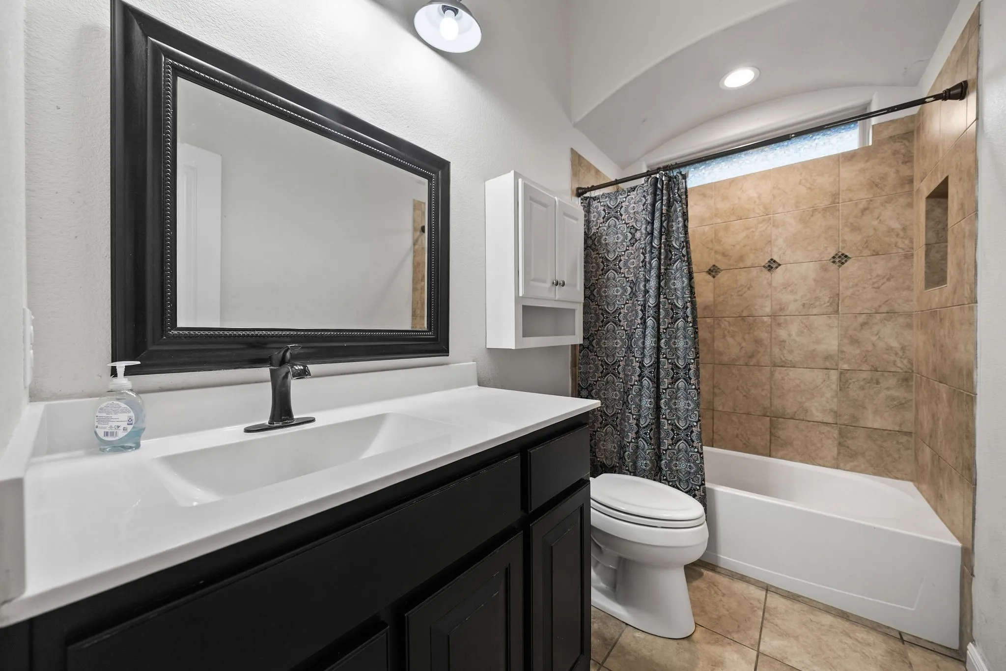 Bathroom featuring a dark wood-finish vanity with a white integrated sink, a framed mirror, and a shower-tub combination with tiled walls and a recessed niche