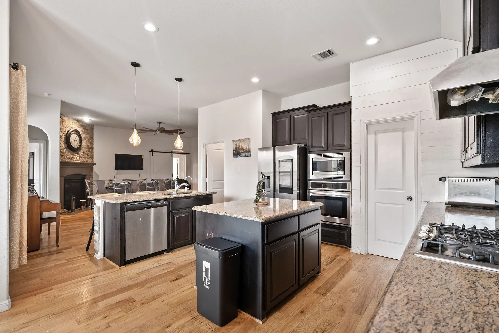 Gourmet kitchen featuring wood-finish flooring, two large islands with granite countertops, dark wood cabinetry, and stainless steel appliances including a double oven and gas range