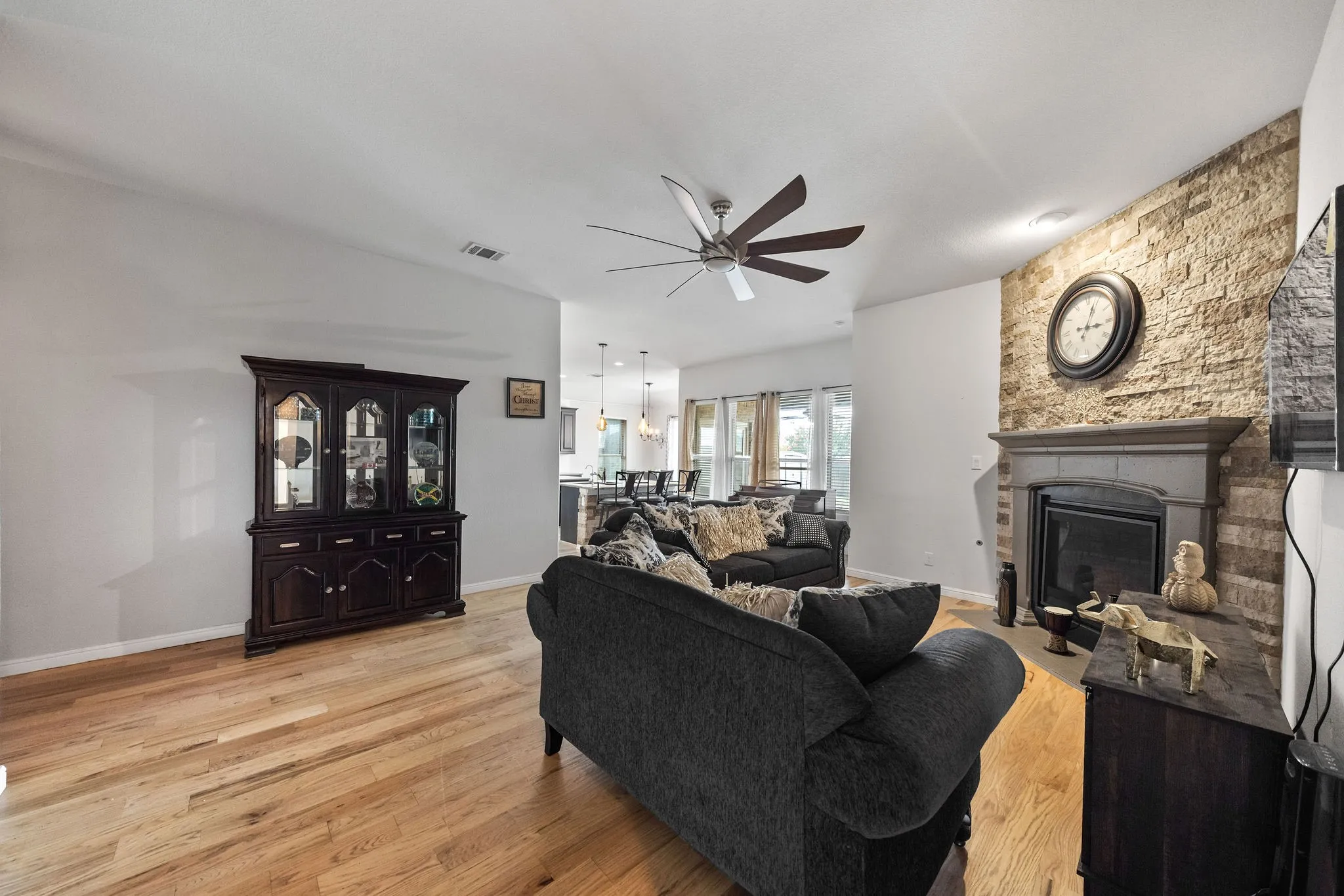 Living area featuring wood-finish flooring, a stone-clad fireplace, and a ceiling fan
