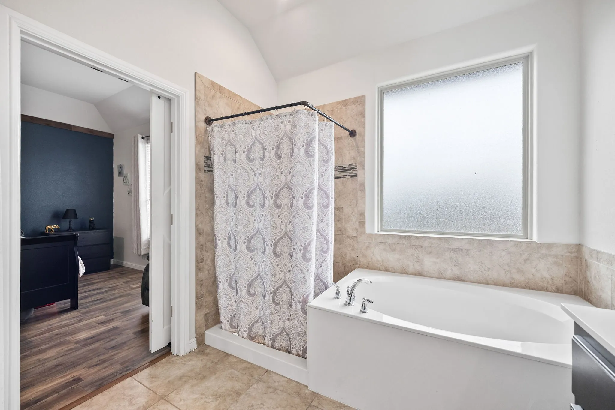 Bathroom featuring a built-in soaking tub with chrome fixtures, a shower with tile surround, and a frosted window