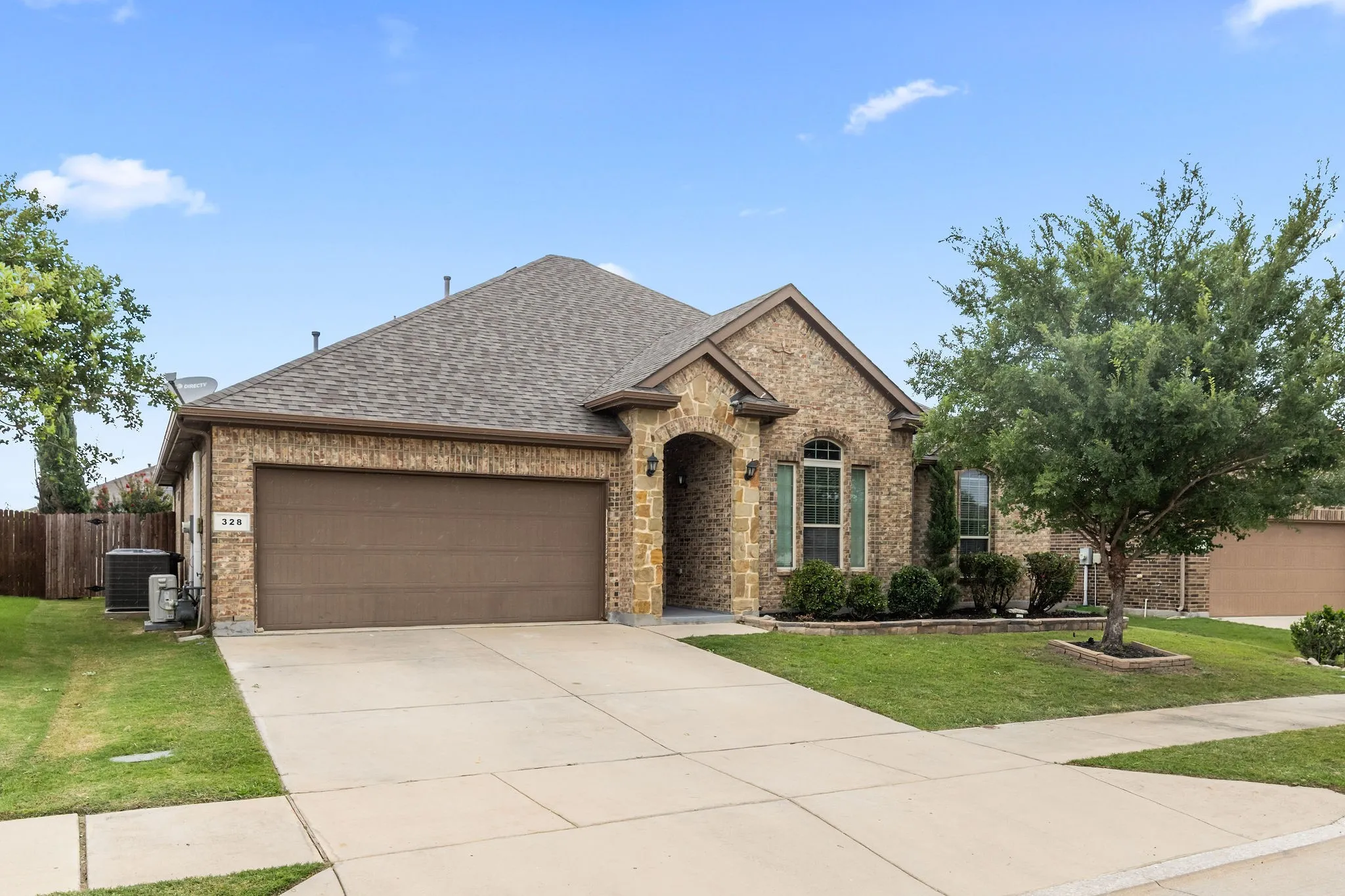 Brick and stone facade residence featuring a two-car garage, arched entryways, a manicured lawn, and mature landscaping