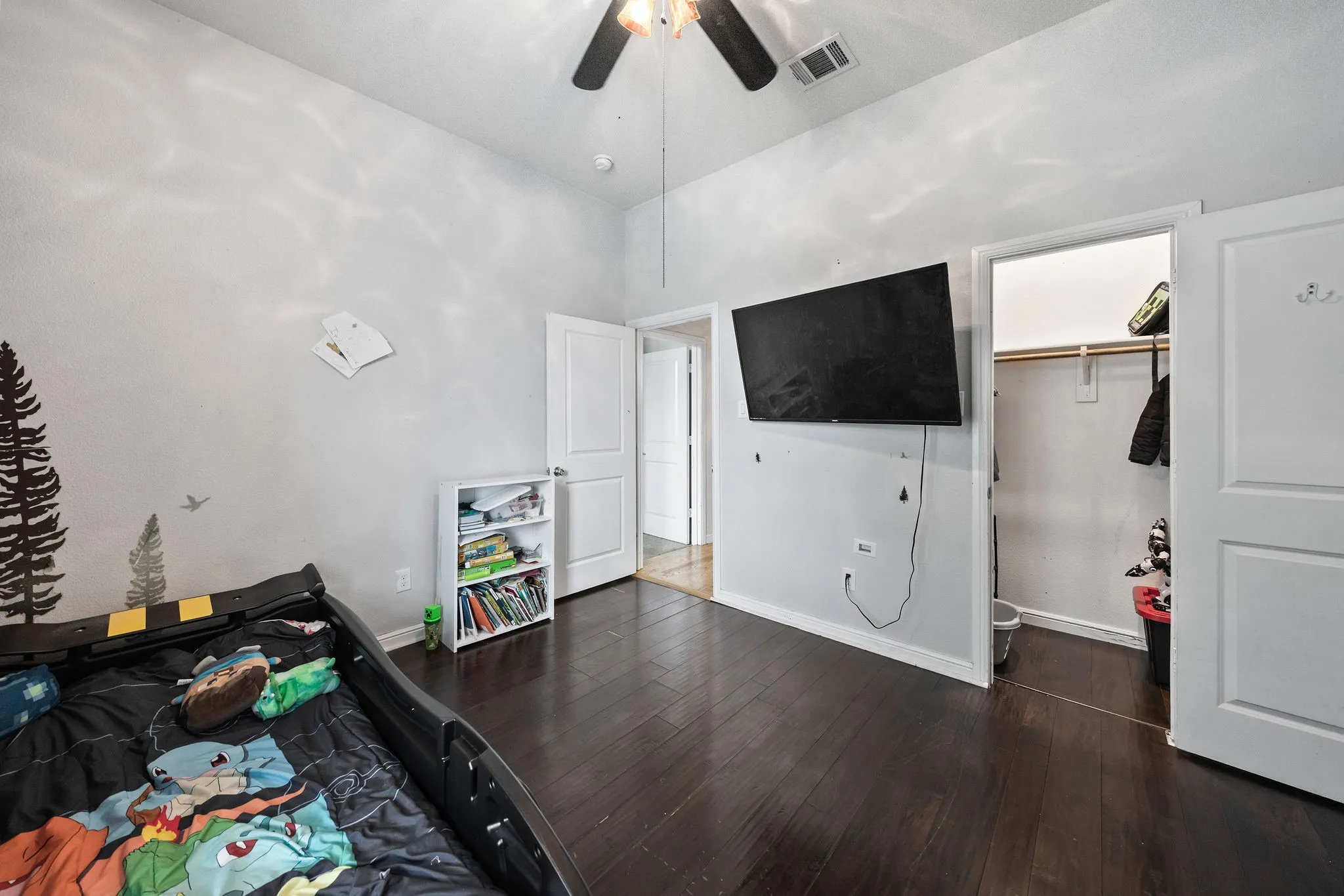 Room featuring dark wood-finish flooring, a ceiling fan, and a walk-in closet with shelving