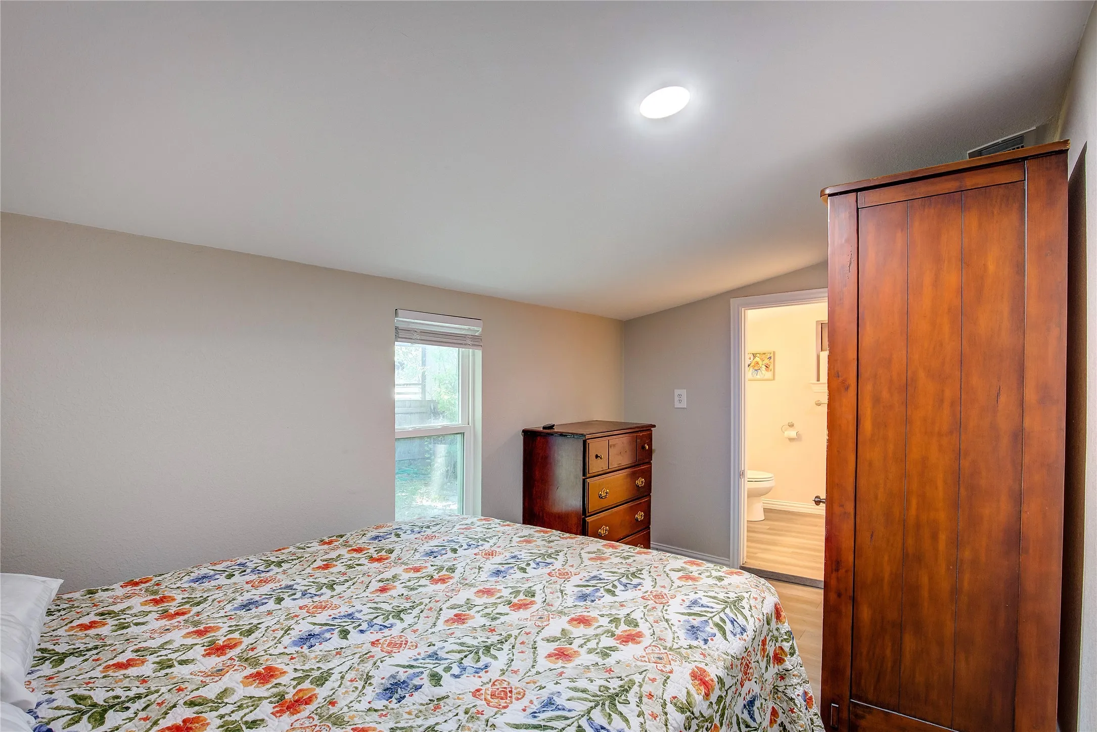 Bedroom featuring light wood-style floors, vaulted ceiling, and connected bathroom