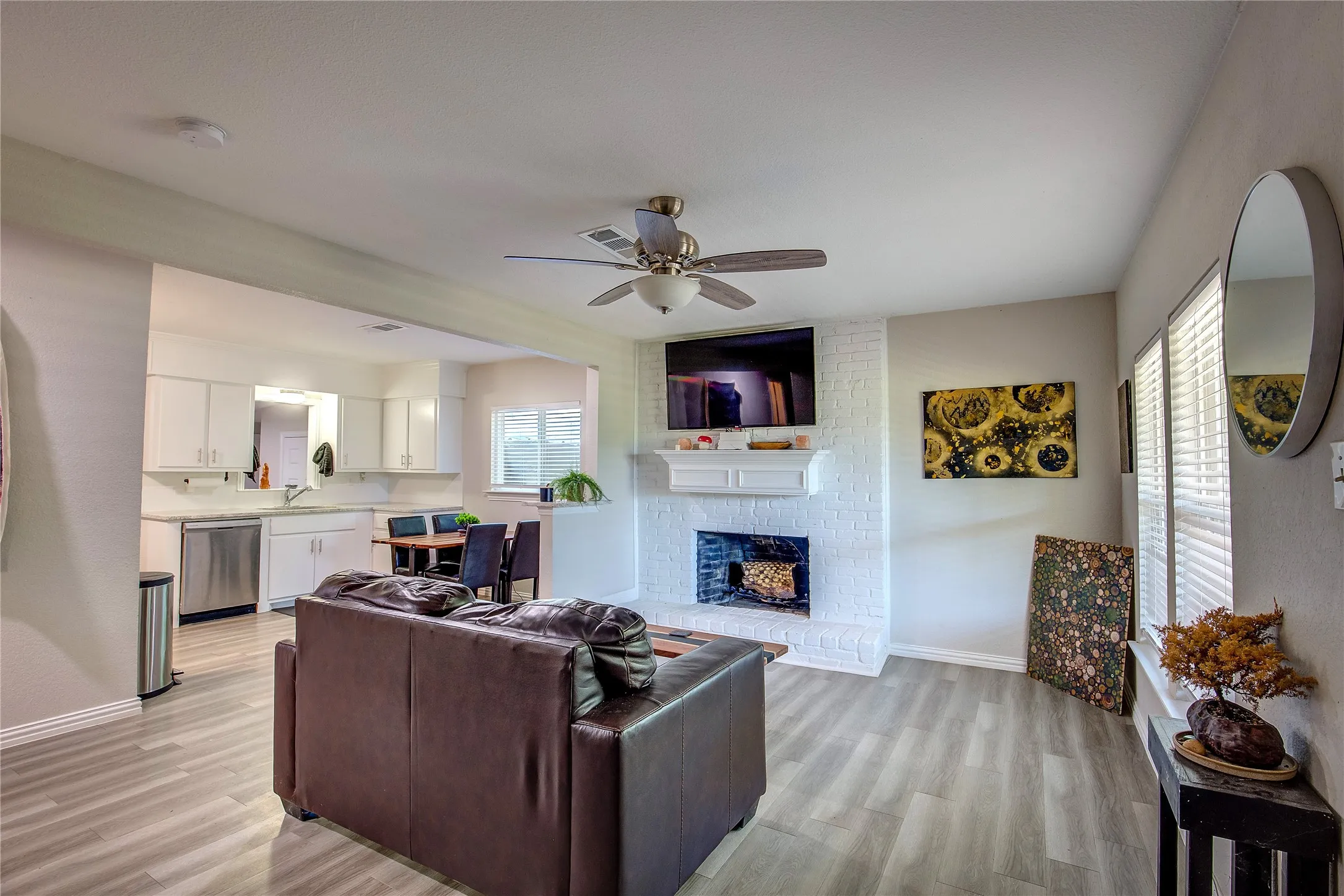 Living area with ceiling fan, light wood finished floors, and a brick fireplace