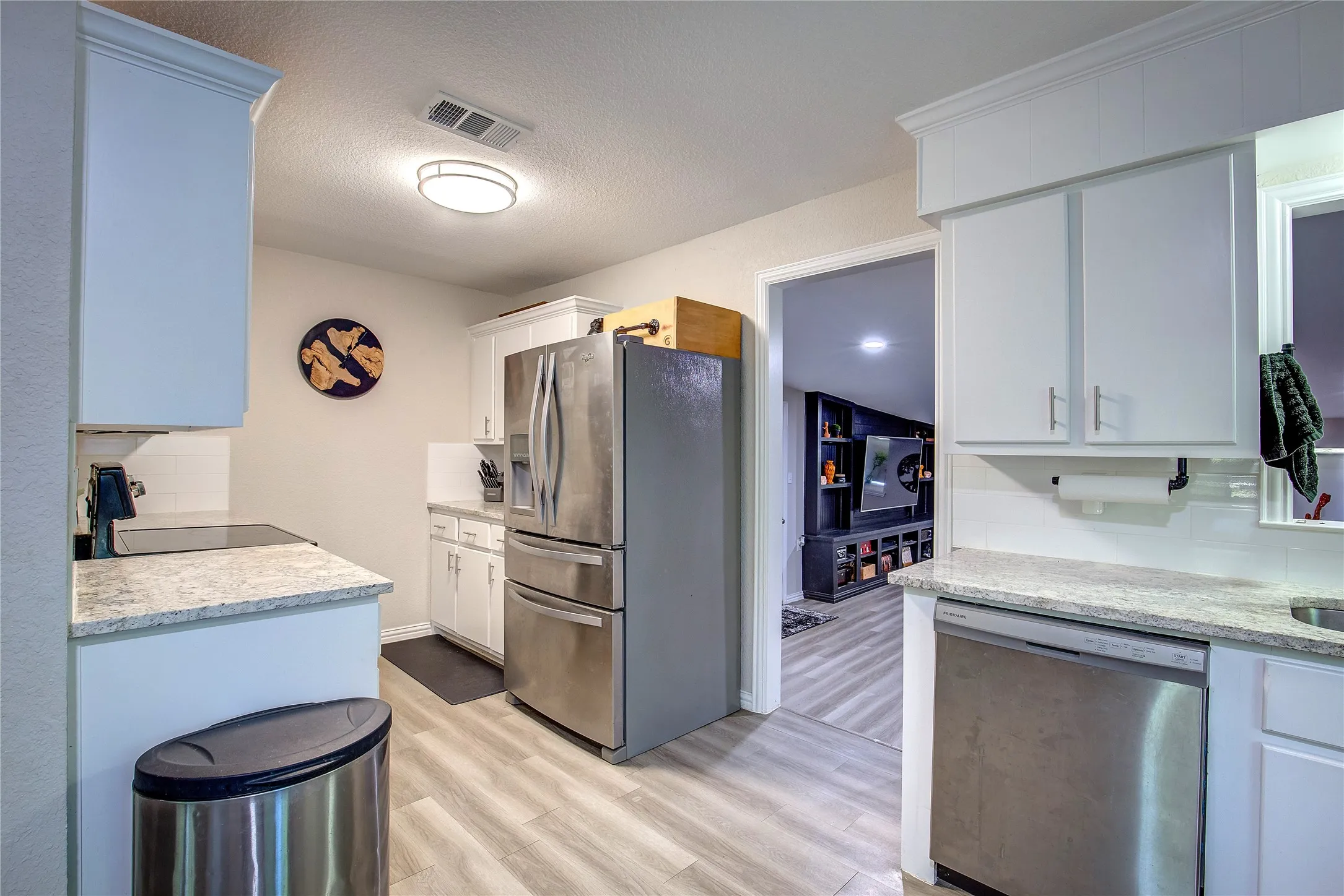 Kitchen featuring tasteful backsplash, stainless steel appliances, light wood-style floors, a textured ceiling, and white cabinetry