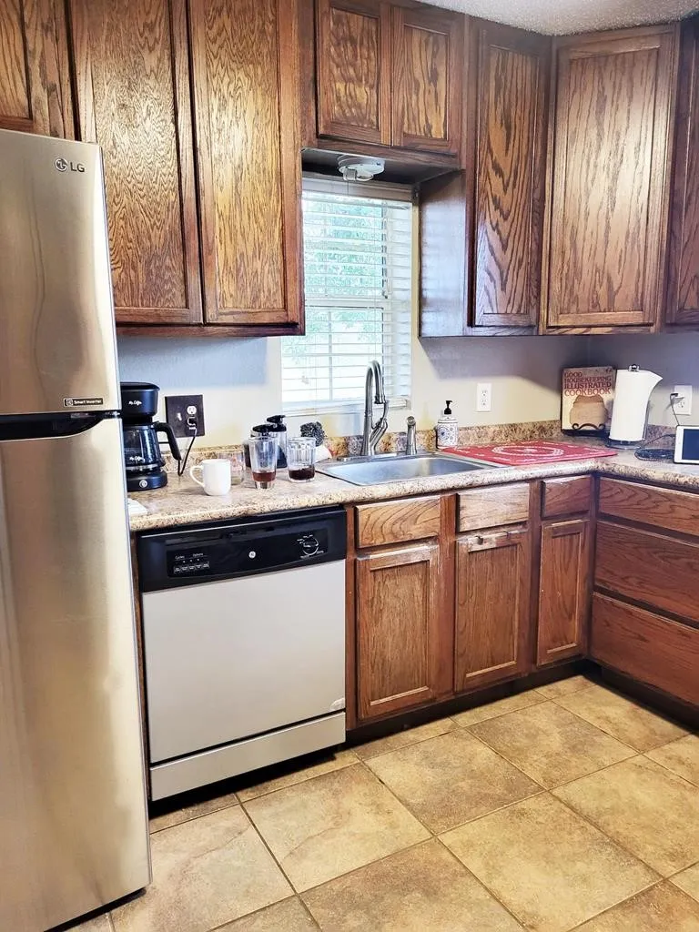 Kitchen featuring wood cabinetry, light-colored countertops, stainless steel refrigerator, and integrated dishwasher