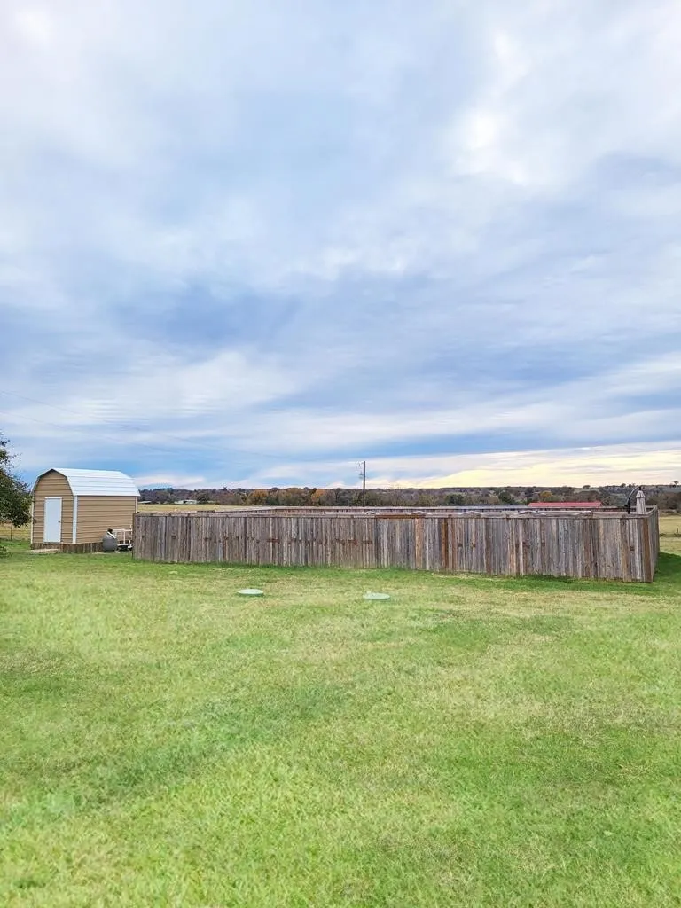 Expansive green lawn featuring a wood privacy fence and a tan storage shed with a white arched roof