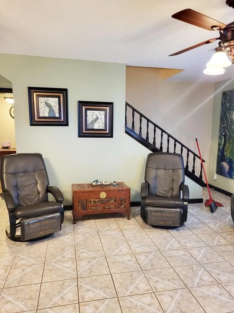 Tiled flooring extends through the space, featuring a staircase with dark wood banister and a ceiling fan with integrated lighting