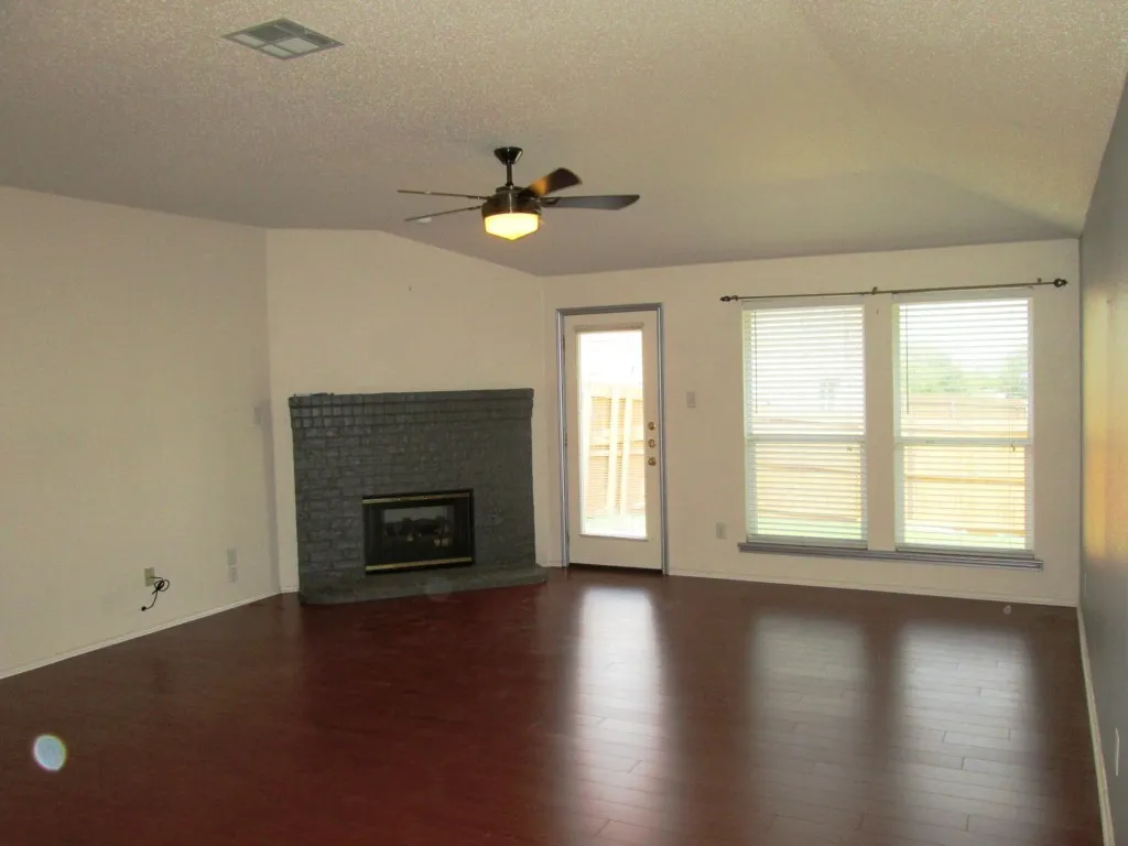 Spacious living area featuring wood-finish flooring, a vaulted ceiling, and a ceiling fan with integrated lighting
