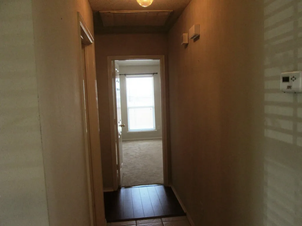 Hallway featuring neutral wall tones, a ceiling-mounted light fixture, and tile flooring with a wood-finish accent mat