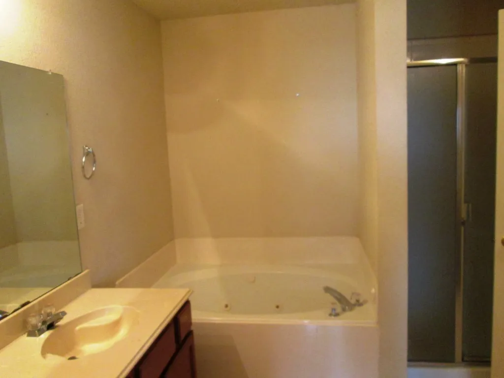 Bathroom featuring a built-in jetted tub, vanity with integrated sink, wall-mounted mirror, and a separate shower enclosure