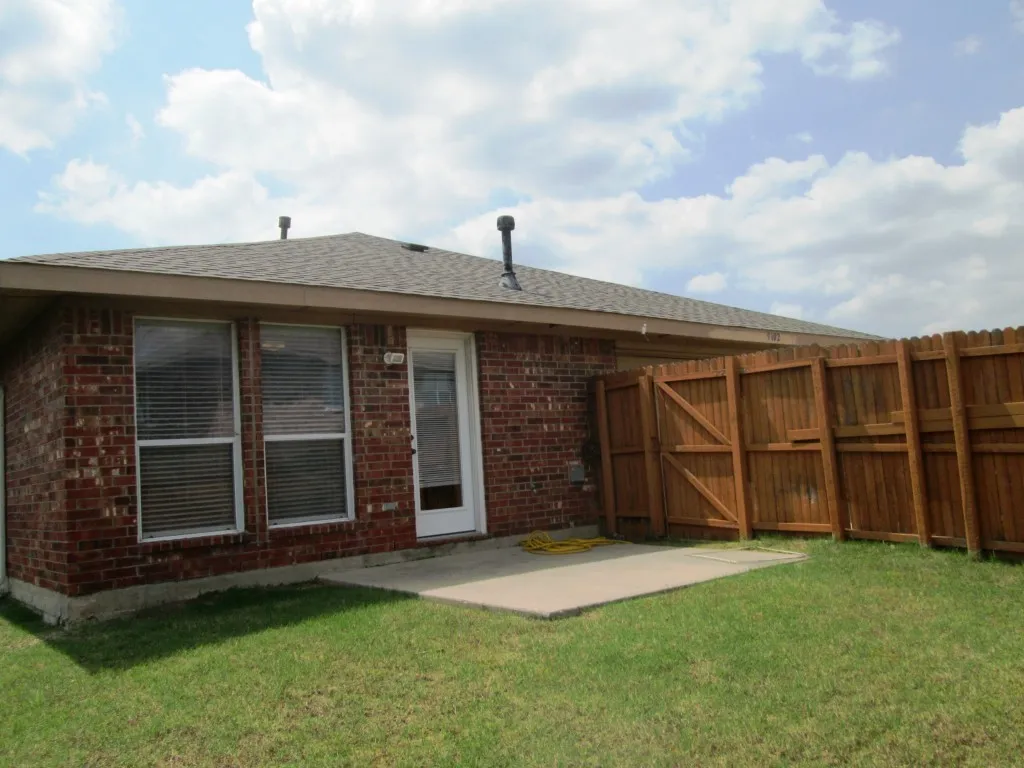 Brick exterior featuring a private wood fence, a concrete patio, and a grass lawn