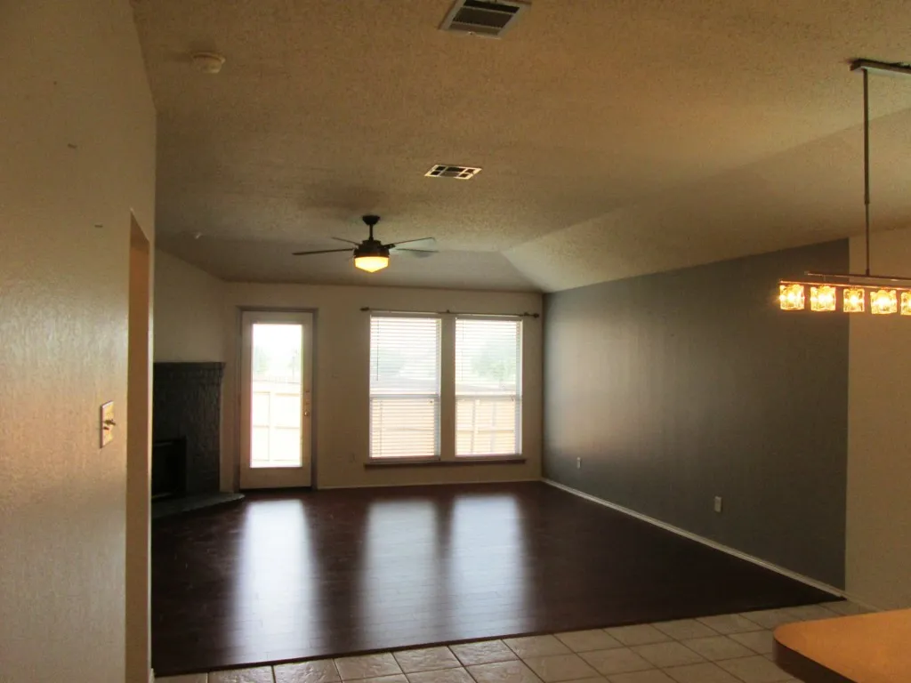 Living area featuring dark wood-finish flooring, a vaulted ceiling, and a ceiling fan with integrated lighting
