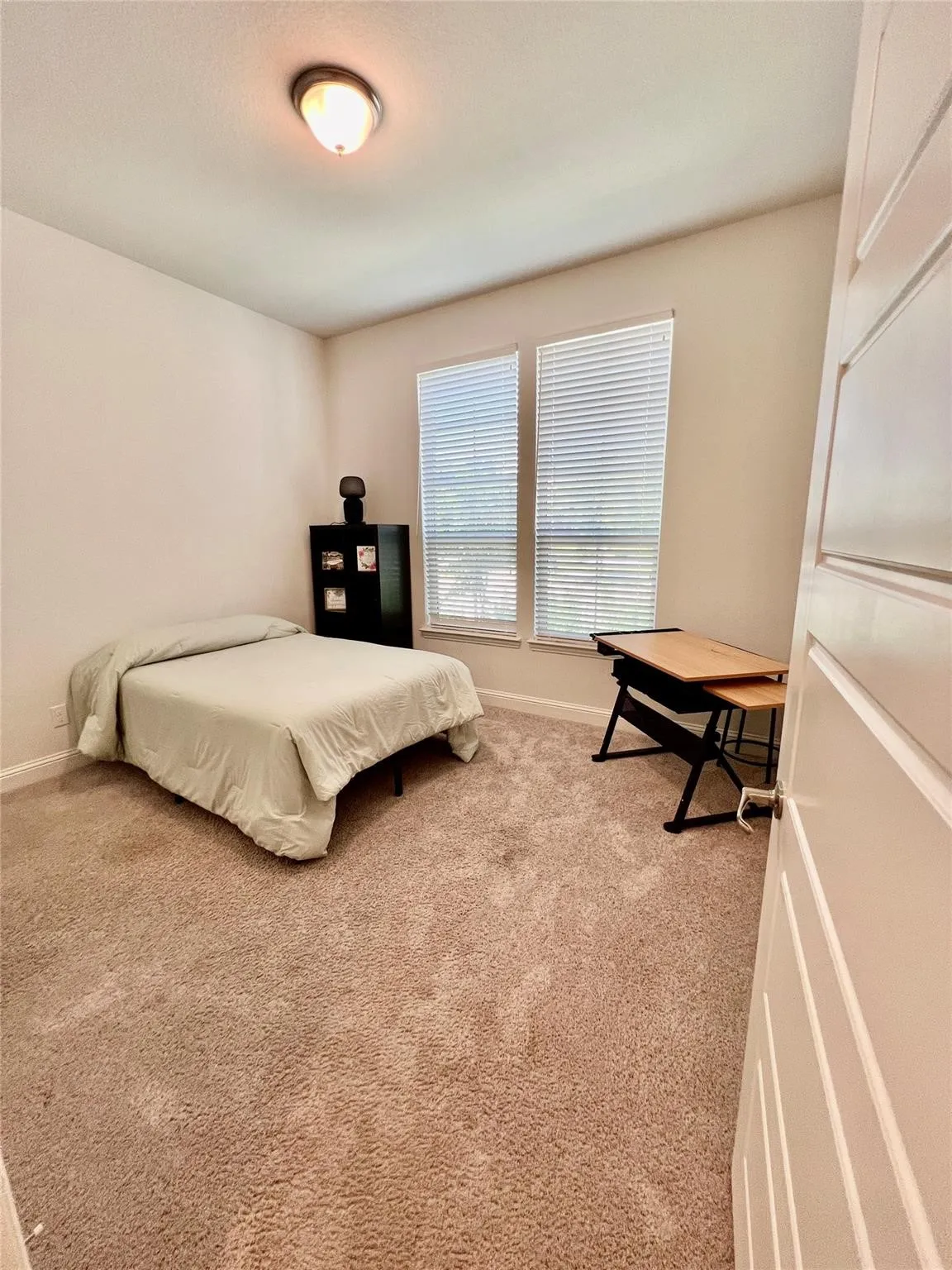 Plush carpeting in a neutral tone grounds this room, featuring two windows with horizontal blinds for adjustable light control