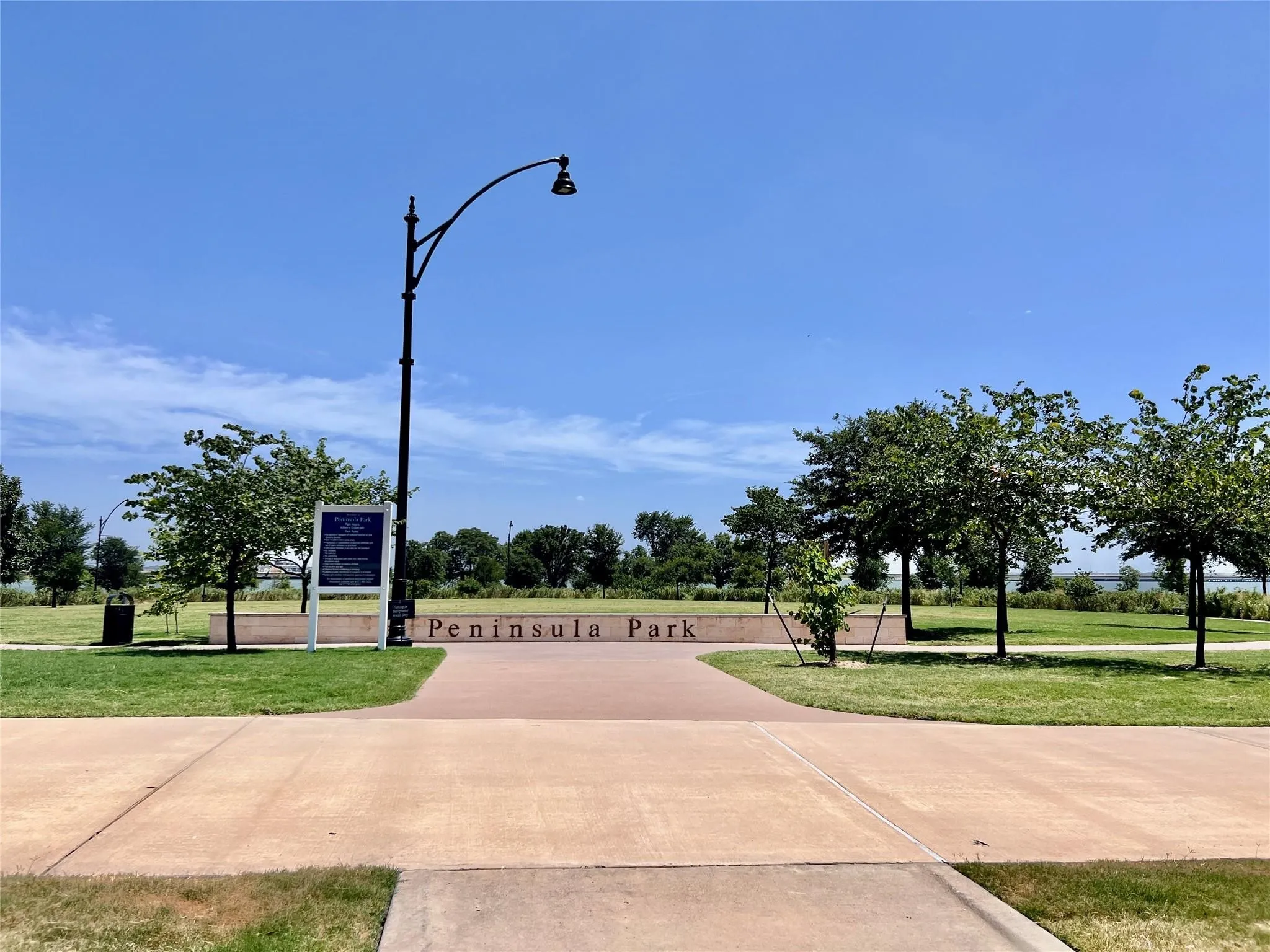 Paved park entrance featuring a street lamp and lush green spaces